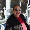 Smiling man wearing sunglasses standing outside near a white fence
