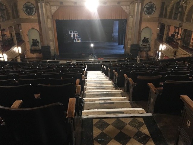 Empty theater auditorium with seats facing a stage, viewed from the backstage area
