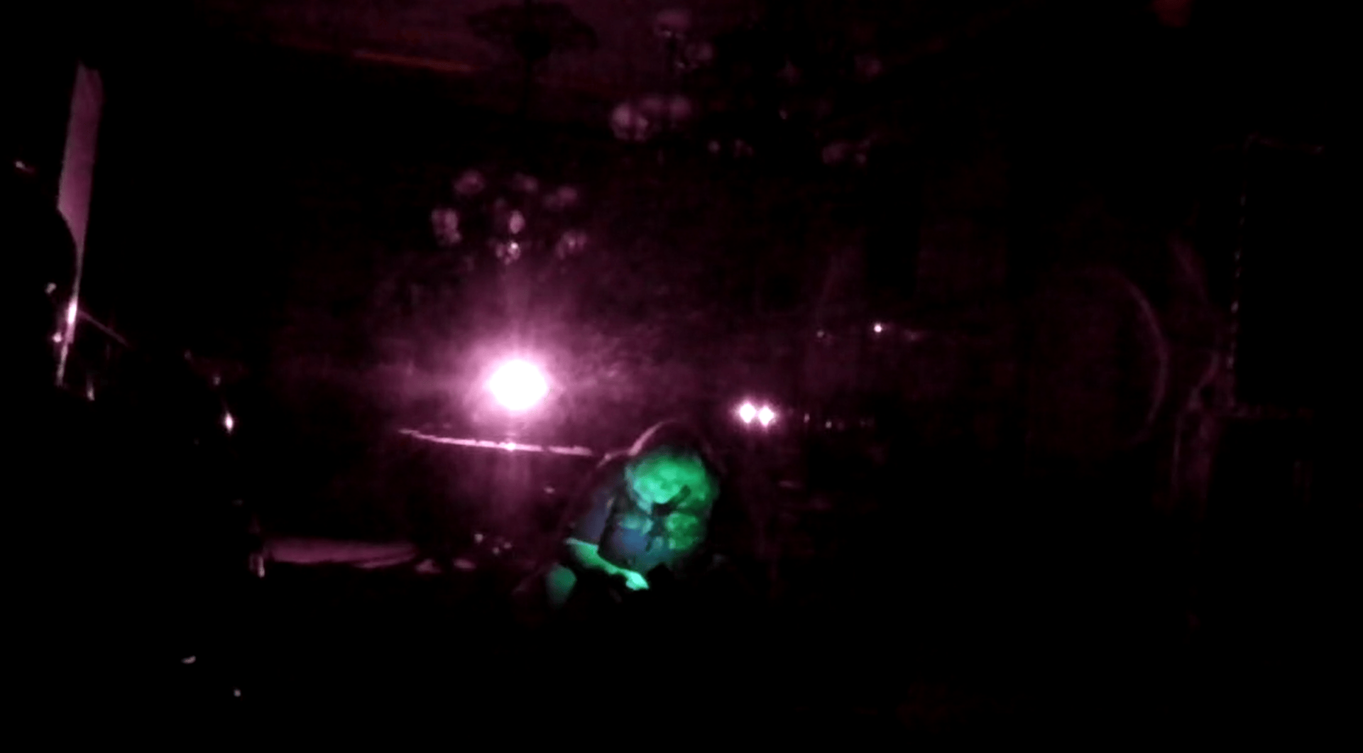 A person sitting in a dark room illuminated by a green light, with purple full spectrum lighting surrounding them.