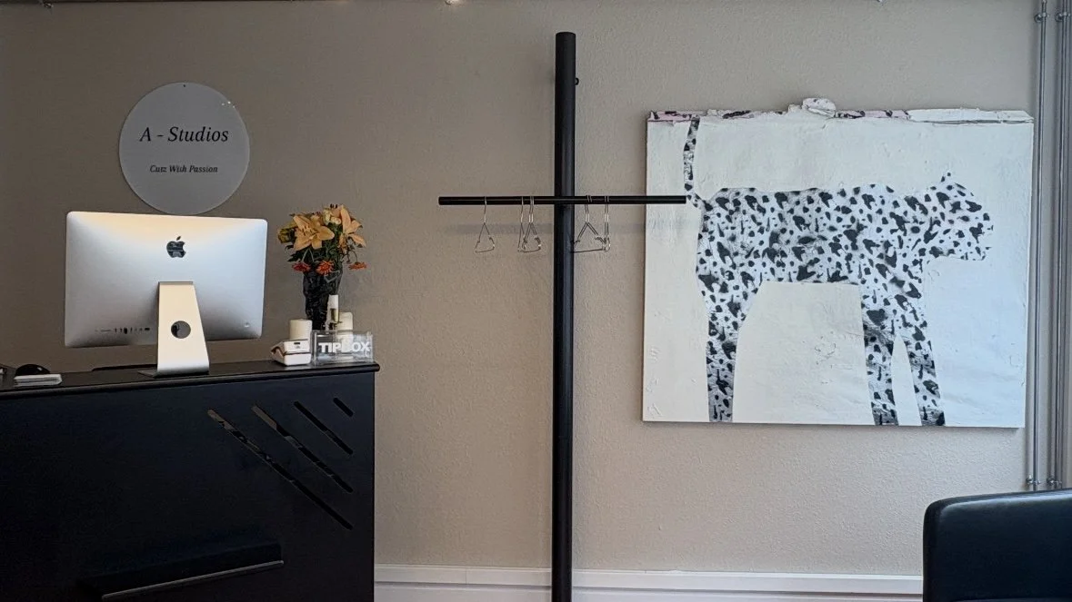 Office reception area with a computer, flowers, and a coat rack in front of a wall with a big painting of a Dalmatian dog.