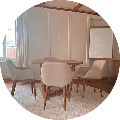 Ein Sitzungsraum mit einem runden Tisch, vier Stühlen, einer weißen Tafel und Vorhängen vor einem Fenster.
