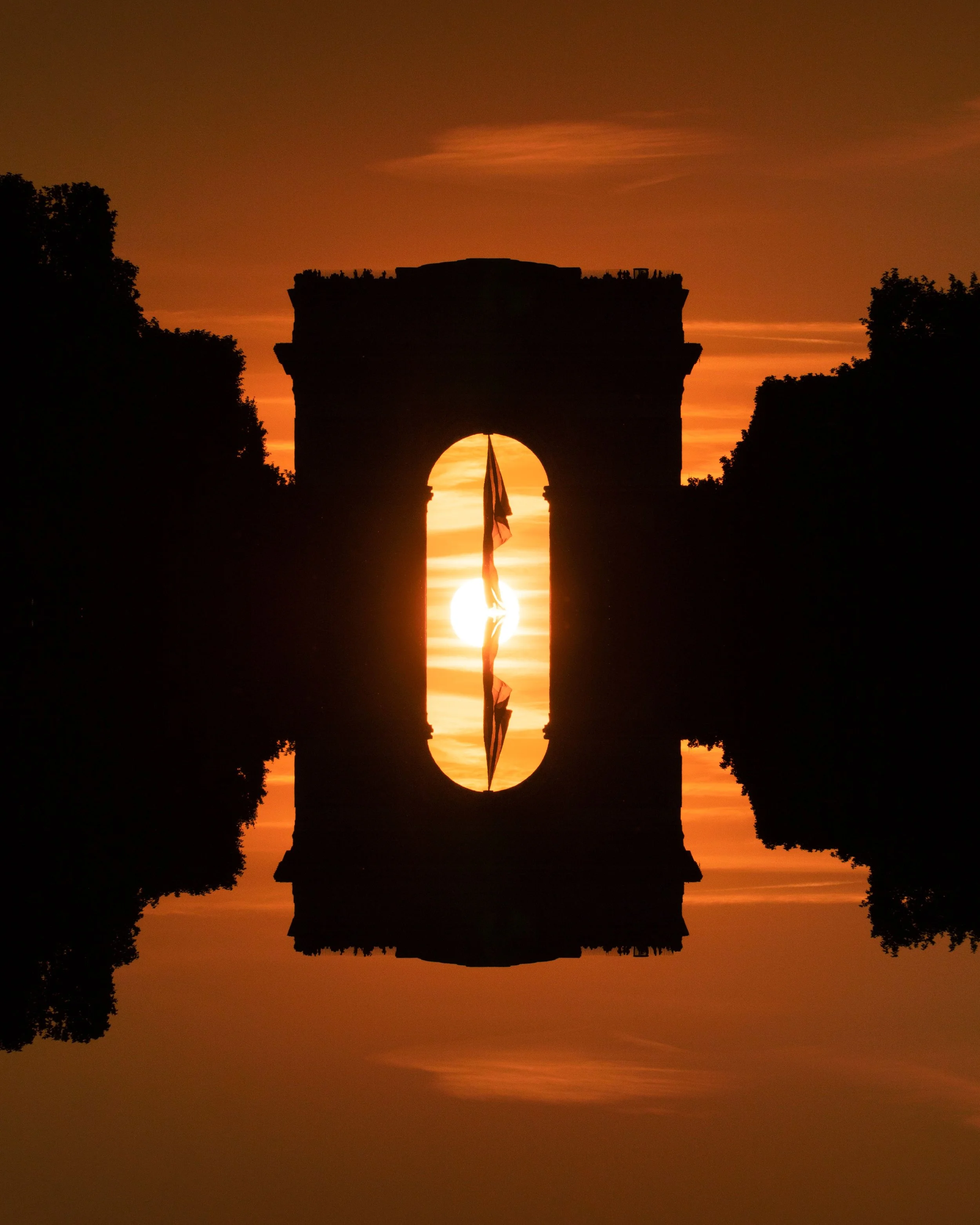 Silhouette de la Puerta de Alcalá en Madrid al atardecer, reflejada en un cuerpo de agua.