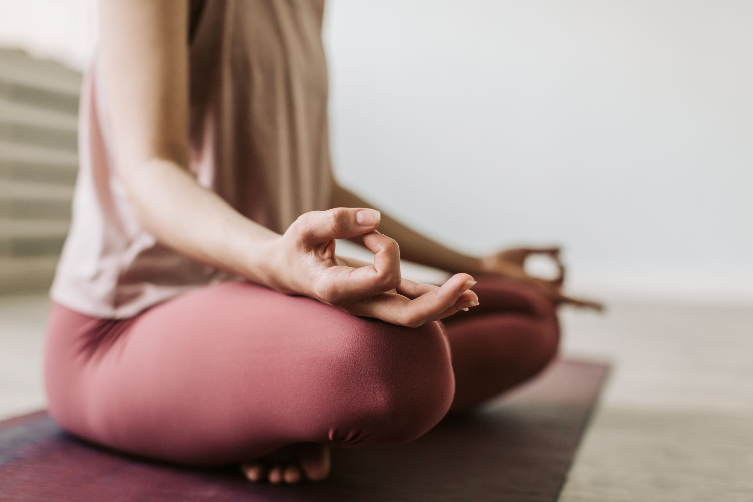 Persona sentada en posición de meditación, con las piernas cruzadas y las manos en posición de 'mudra' sobre las rodillas, en un ambiente interior tranquilo.