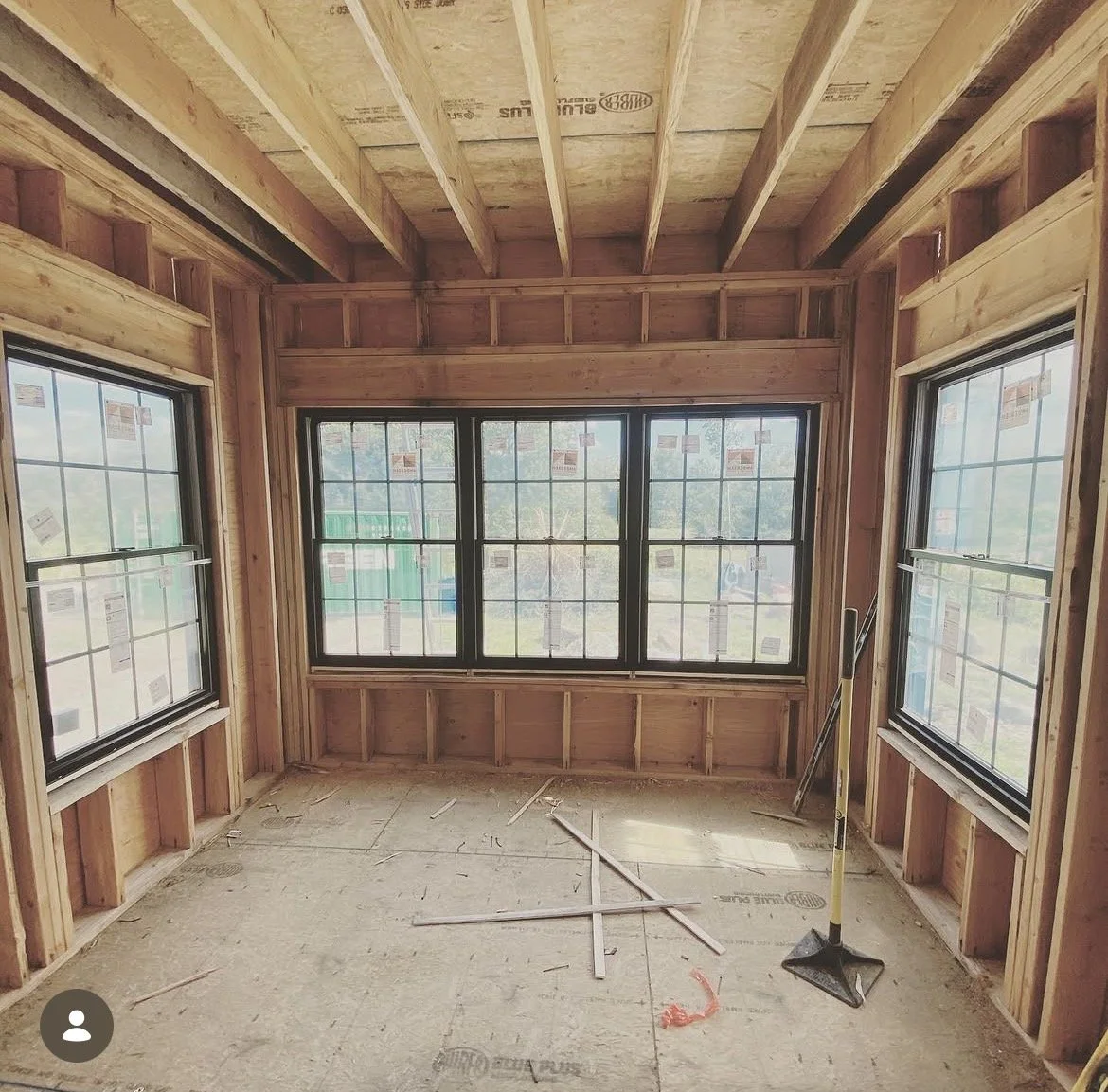 Interior of a room under construction with wooden framing, large windows, and construction tools on the floor.