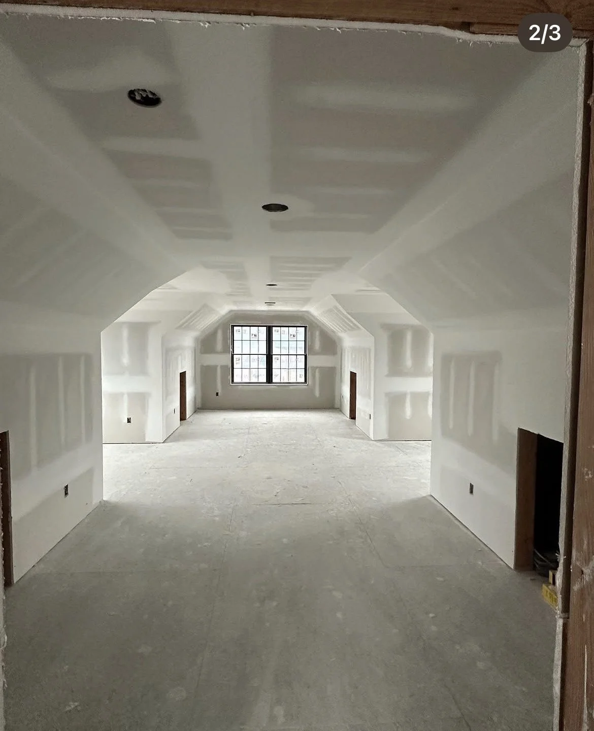 Unfinished attic room with drywall installed, no flooring, and a large window at the far end.