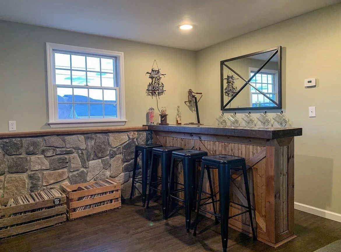 Home bar area with a wooden counter, three black bar stools, a mirror with a black frame, and a window with a mountain view.