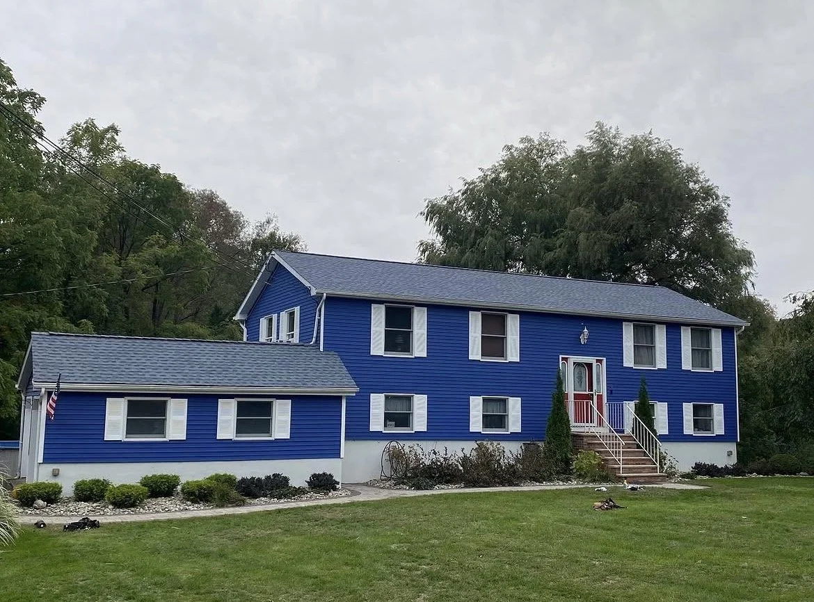A blue two-story house with white trim, a front porch with stairs, and a well-maintained lawn.