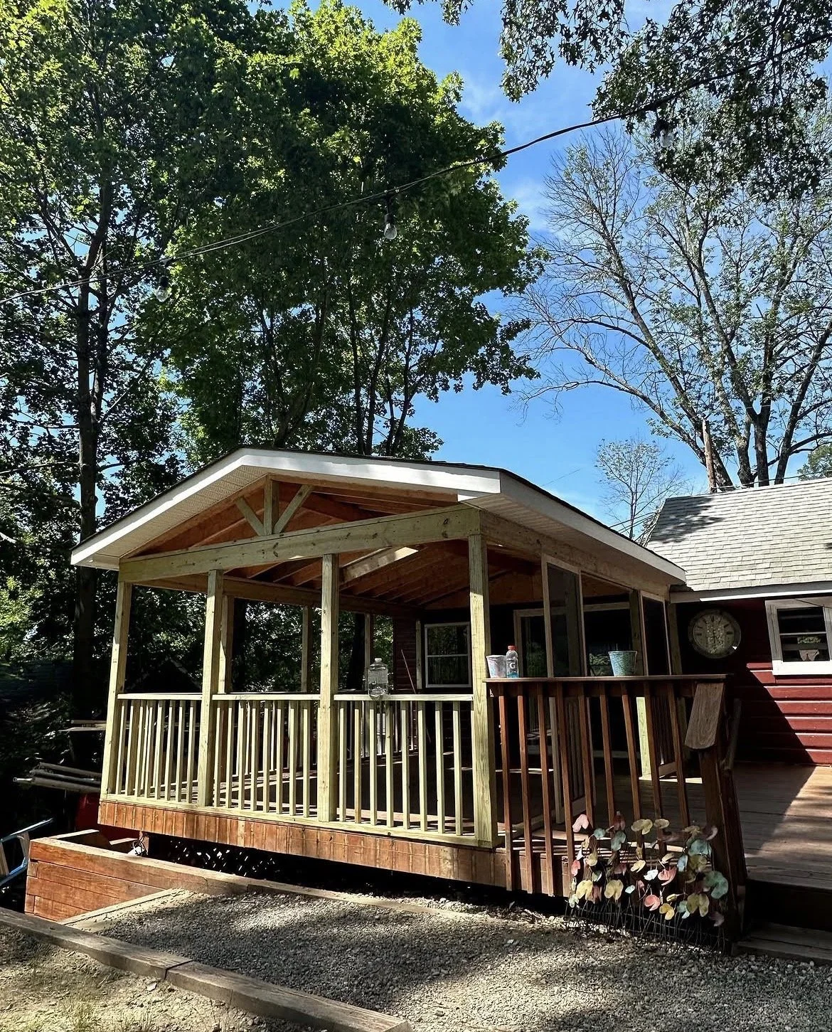 A house with an attached wooden porch that is under construction, with trees and a cloudy blue sky in the background.