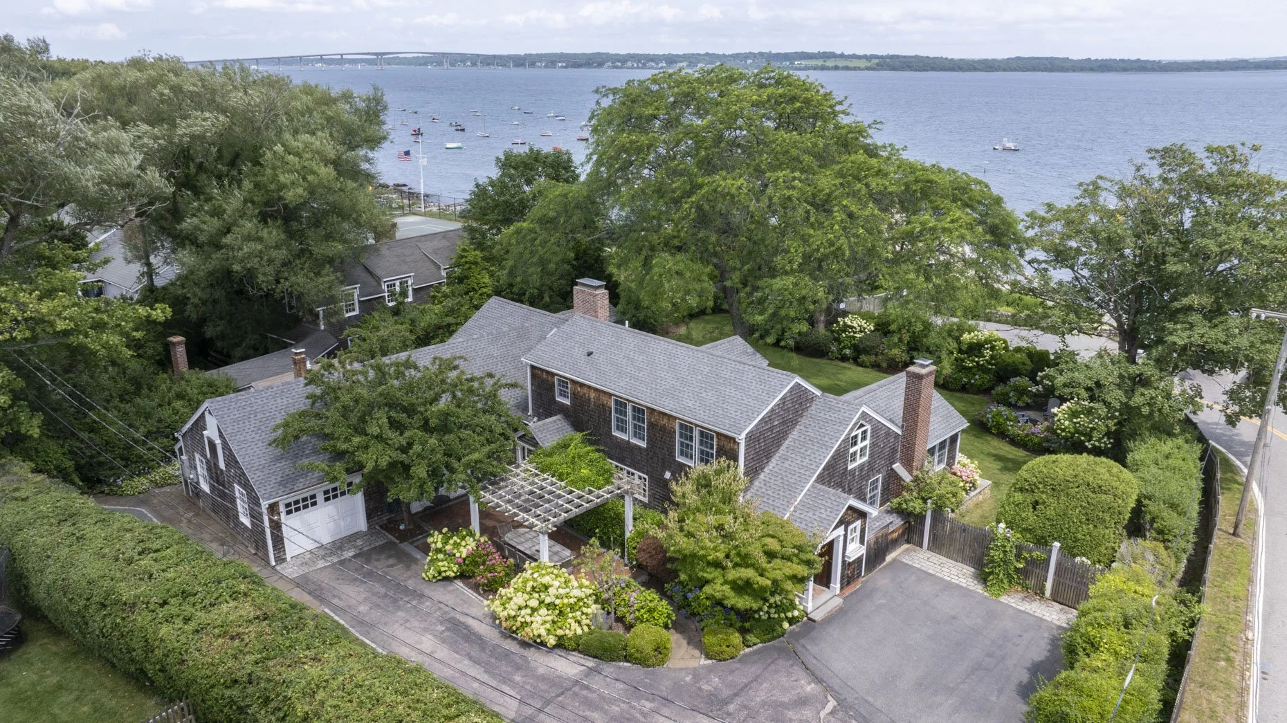 Aerial view of a house by the water with greenery, boats on the water, and a bridge in the background.
