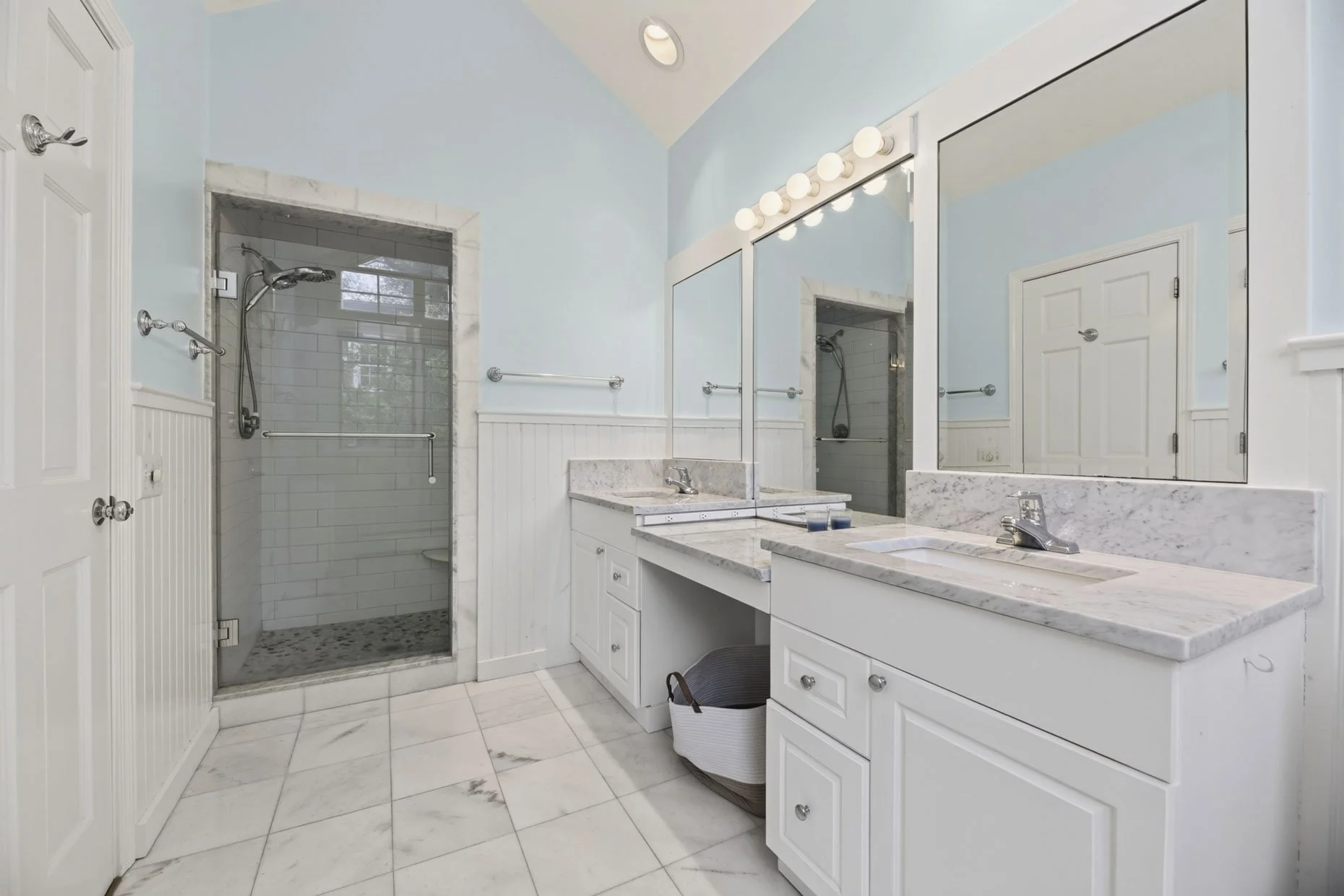 Modern bathroom with white cabinets, marble countertops, large mirror, and a glass shower with white subway tiles.