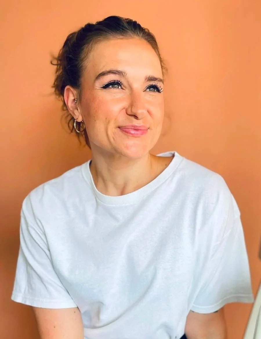 Junge Frau mit kurzen, gebogenen Haaren, die lächelt und einen unscharfen Hintergrund hat.