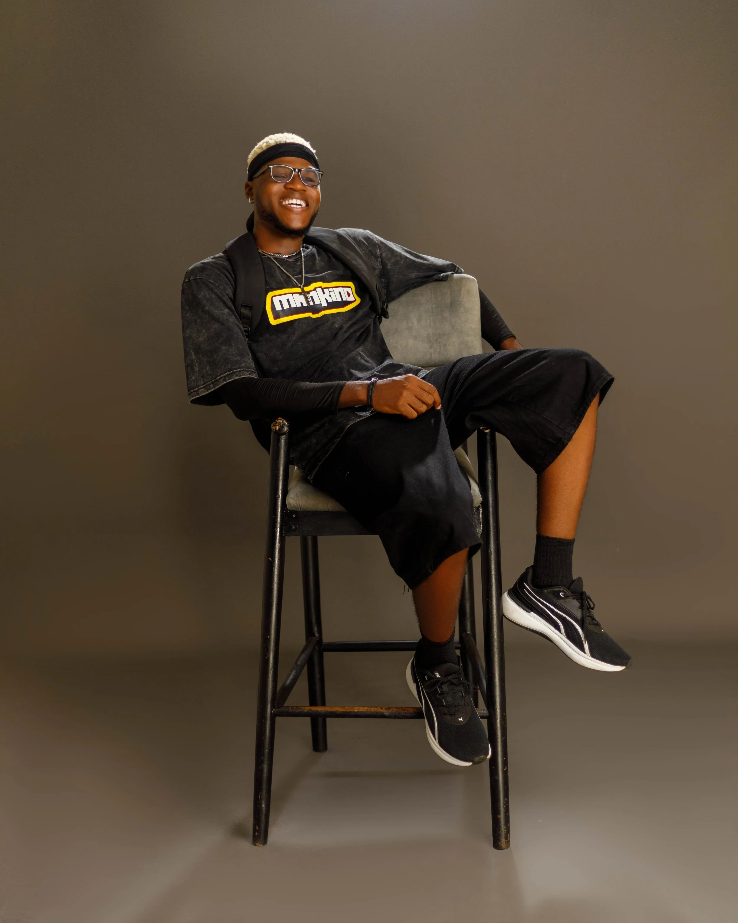 Spyrex seated on a stool wearing MANKIND clothing against a grey background