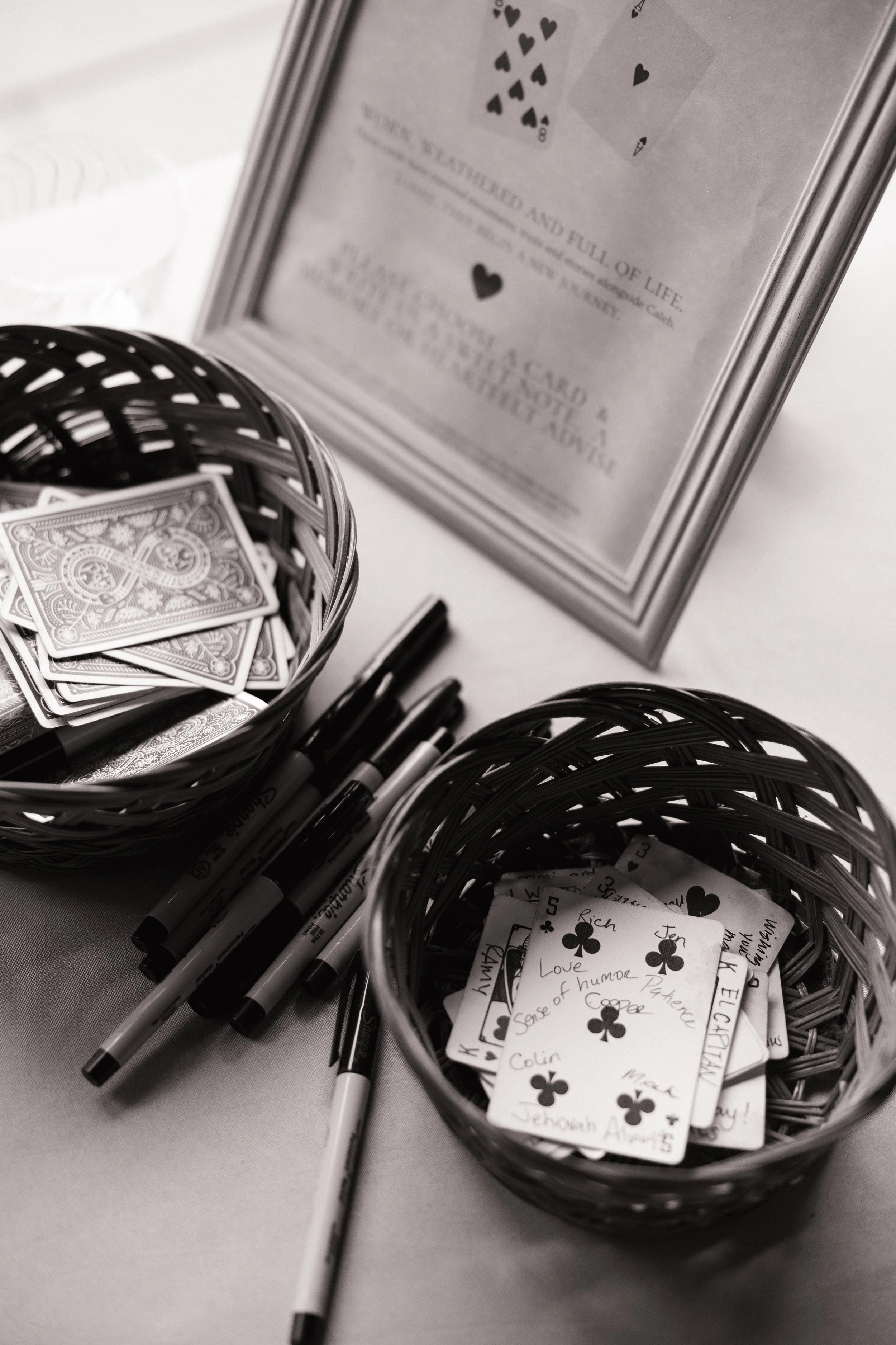 Baskets of playing cards, markers, and handwritten notes with names and messages for a game or activity on a table.