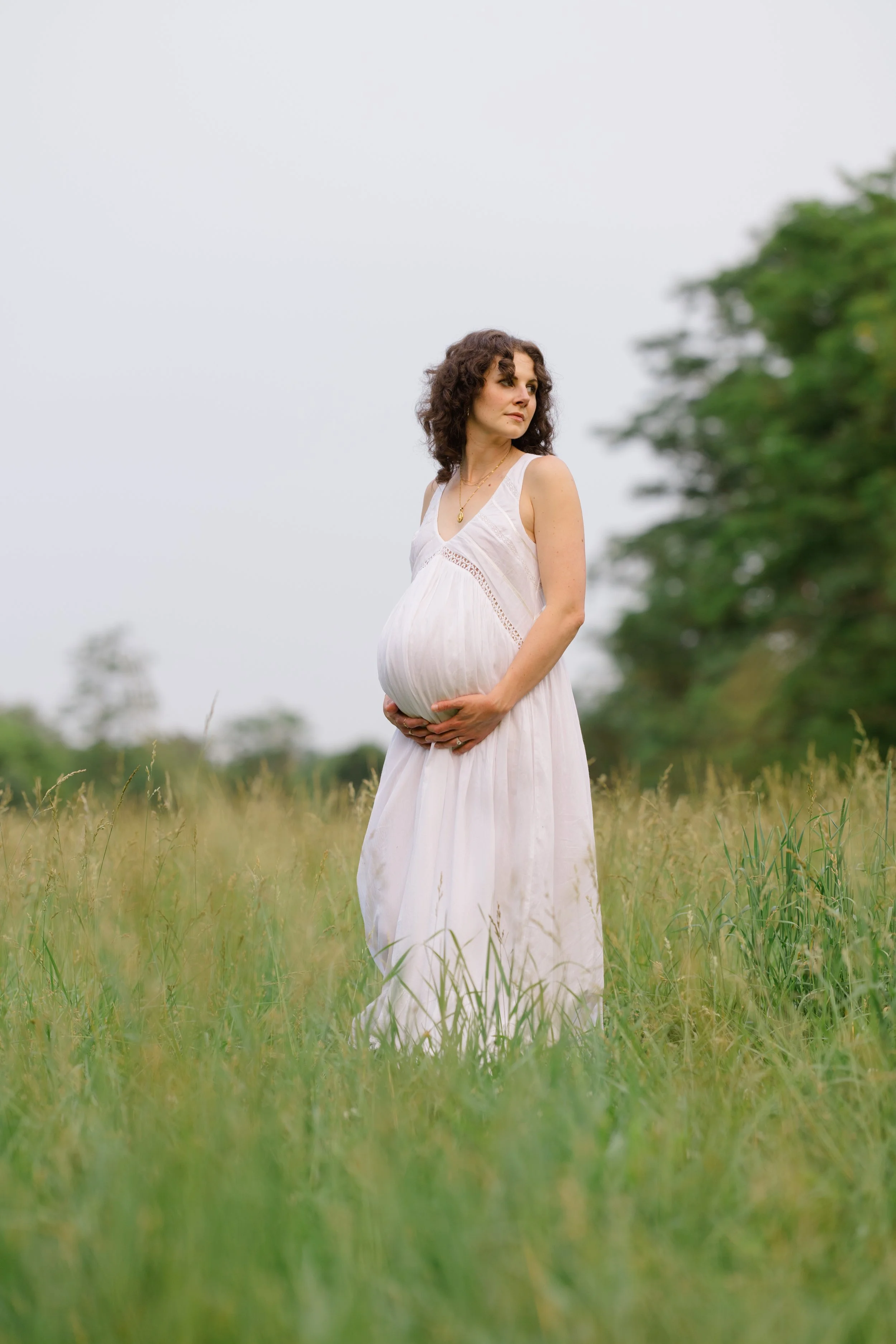 A pregnant woman wearing a white dress standing in a grassy field.