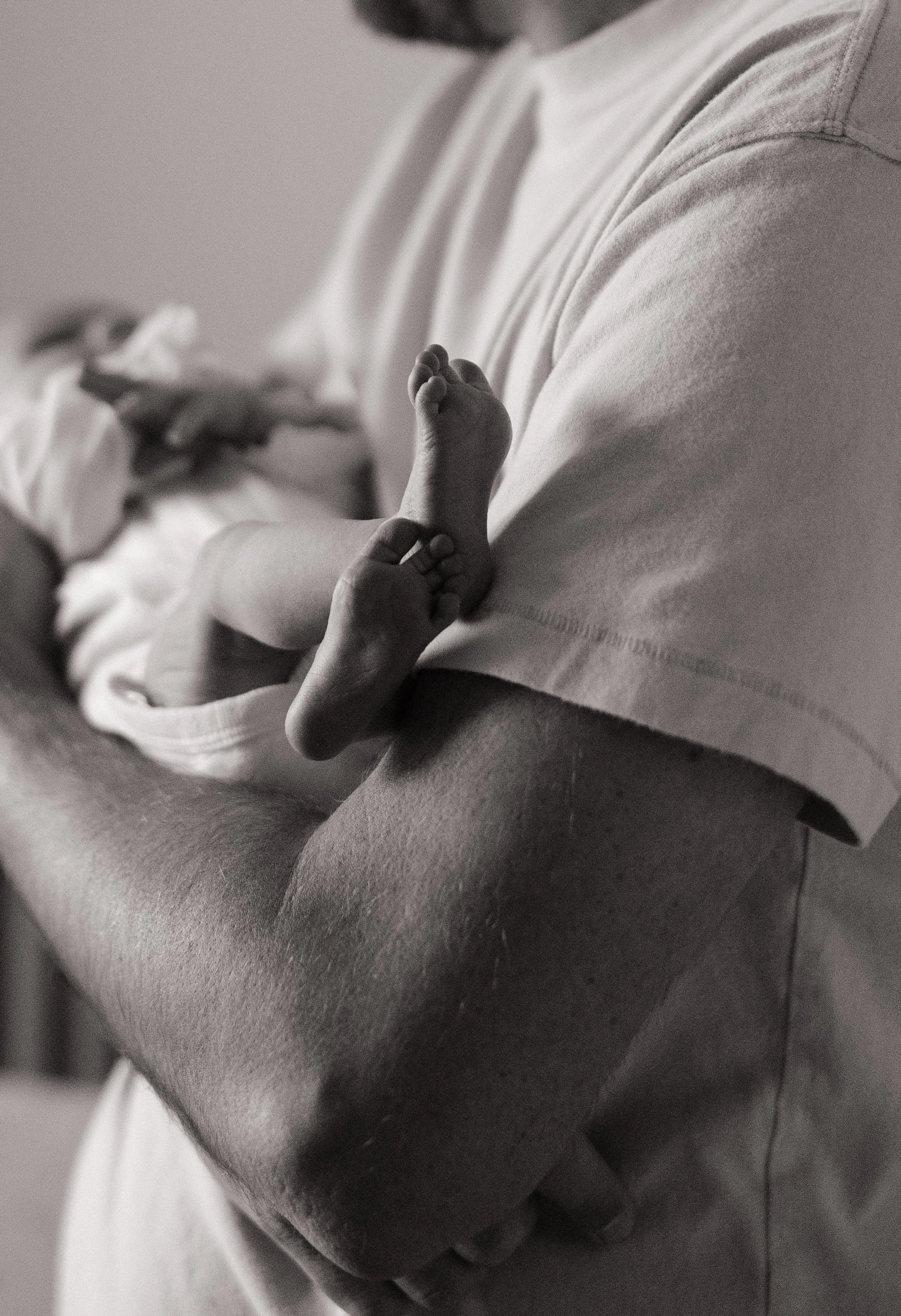 A baby being held in an adult's arms, with one tiny hand grasping an adult's finger.