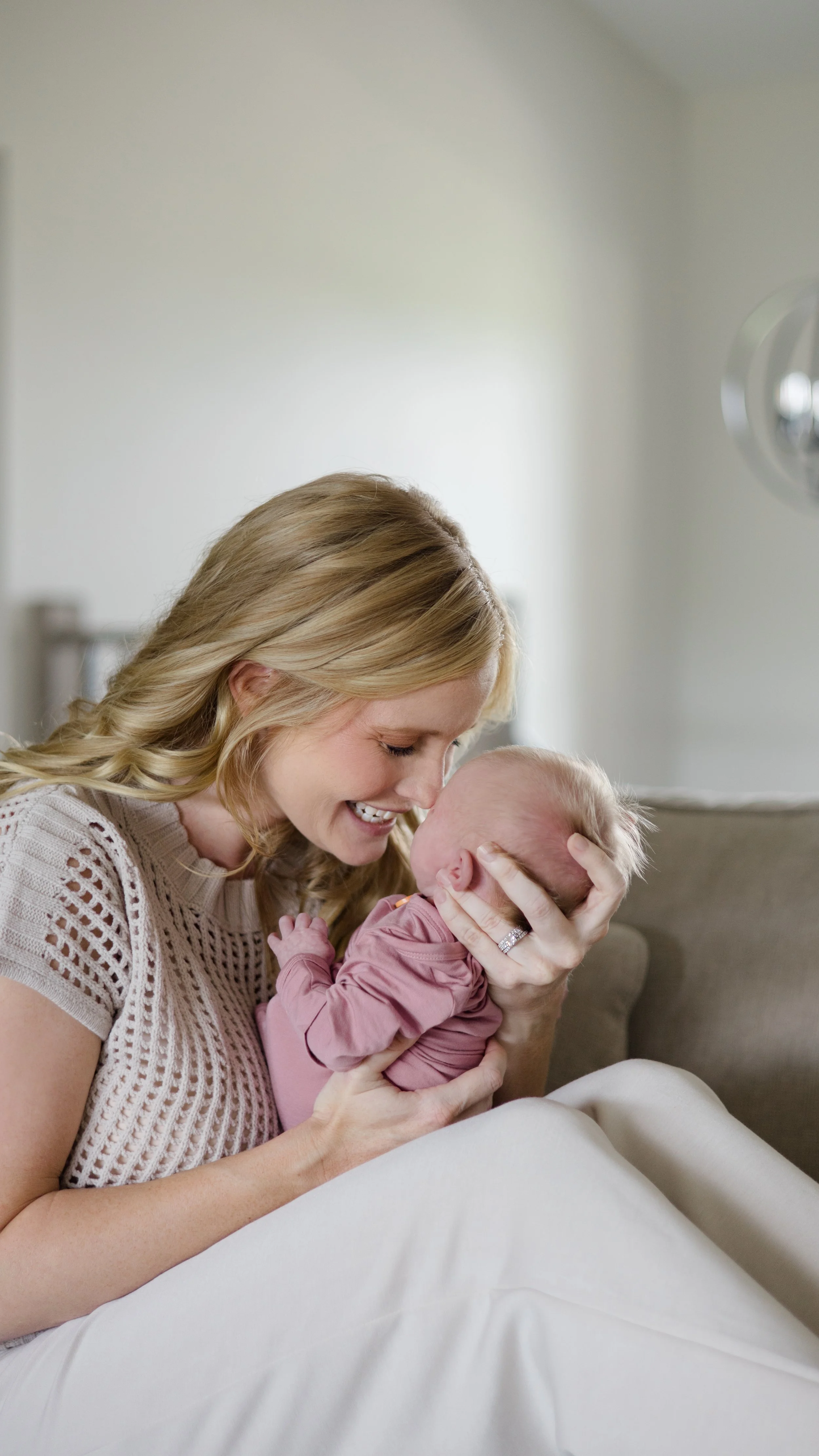 A woman smiling and holding a baby close to her face, both appearing happy, in a cozy indoor setting.