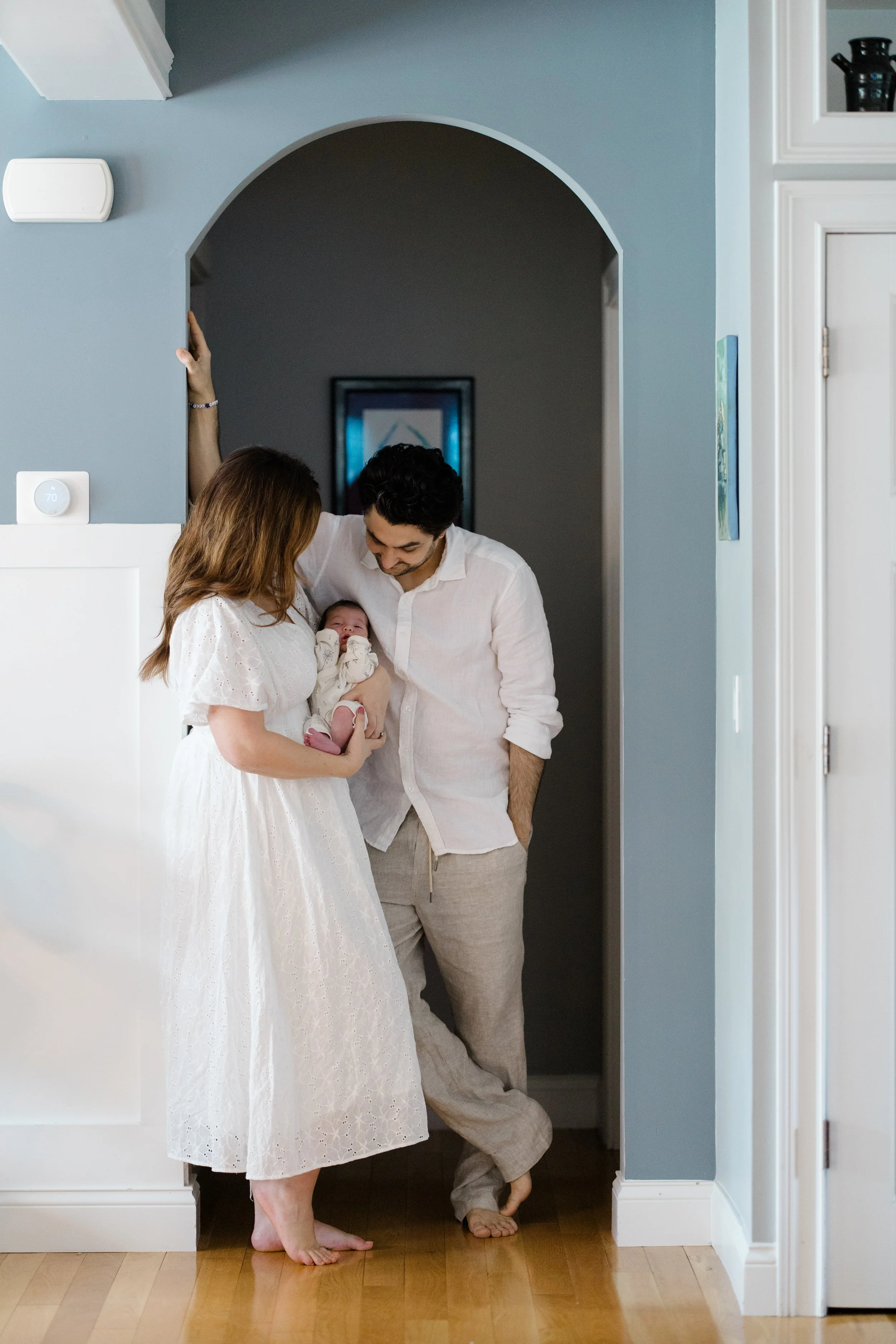 Family in white clothing with a baby standing in a doorway, celebrating, smiling, and touching.