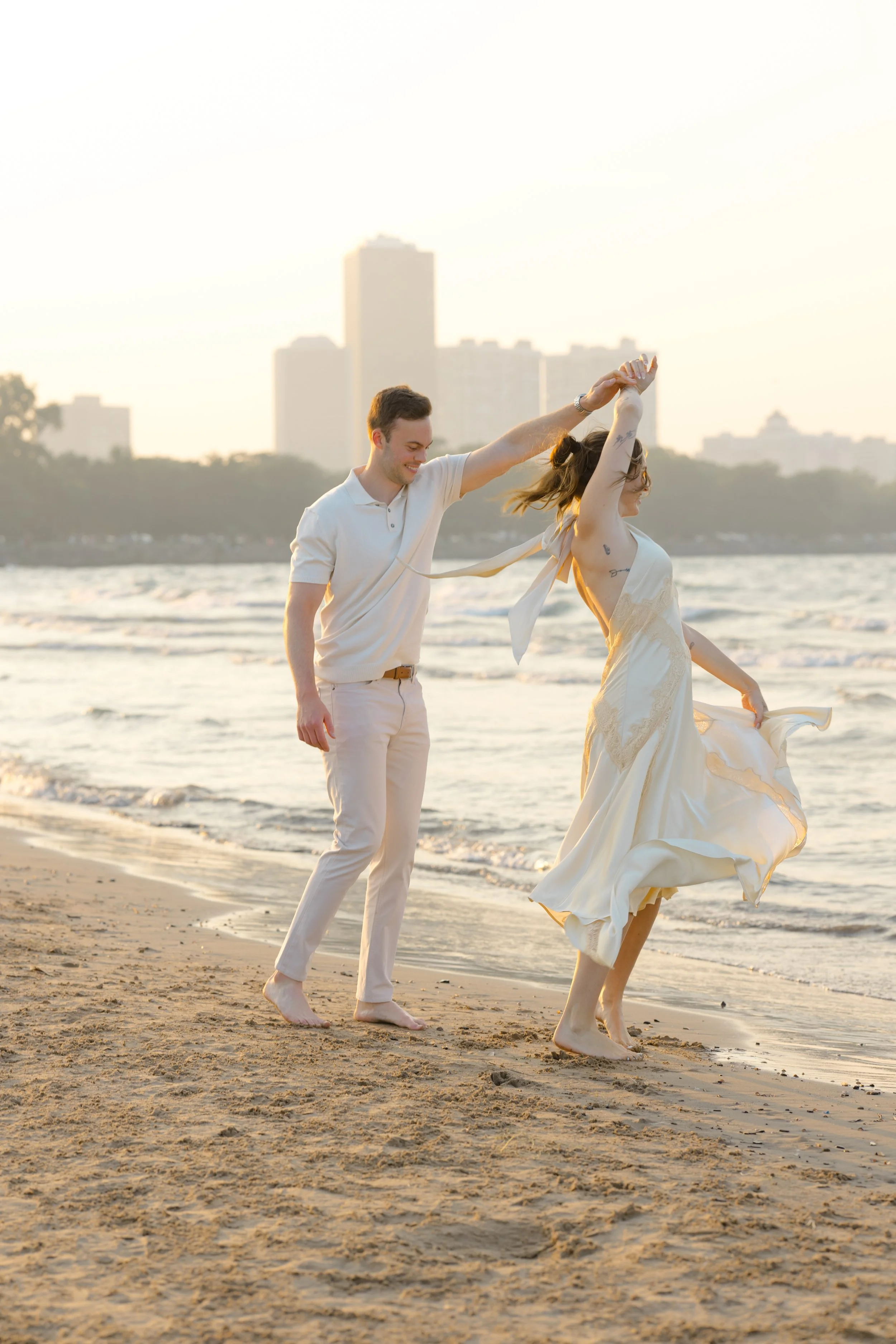 A couple dancing on the beach at sunset, with city skyline in the background.