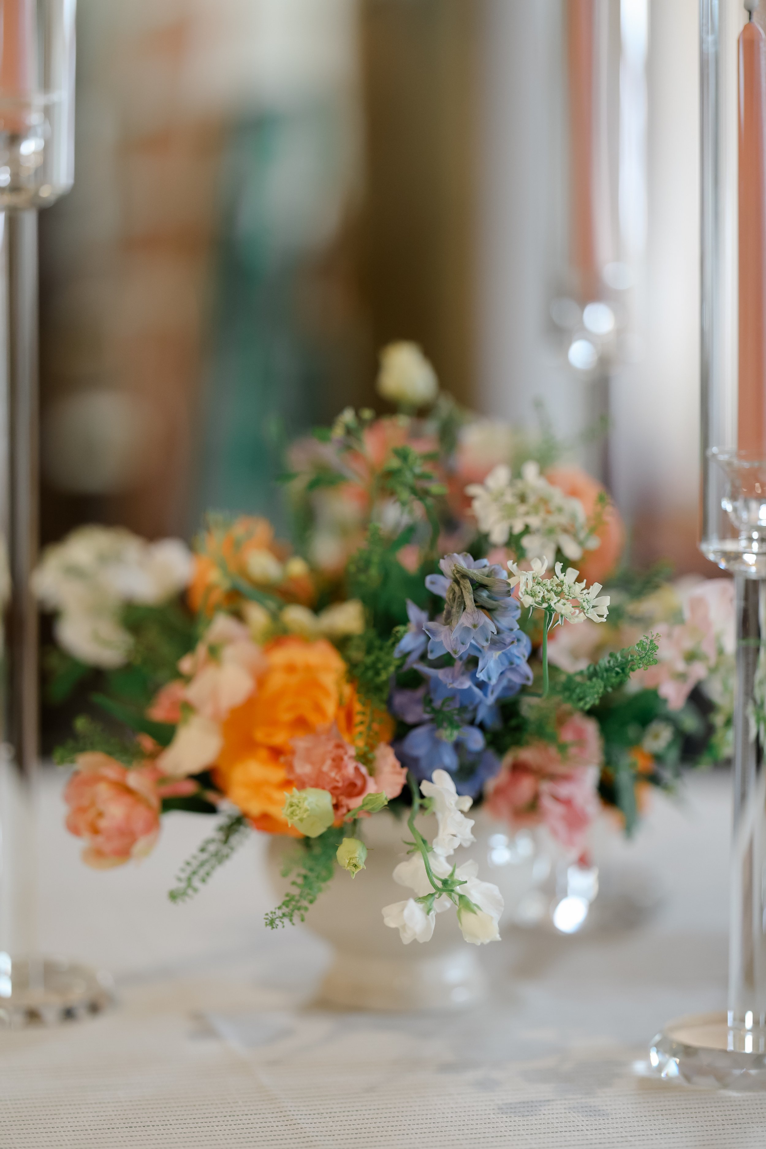 A bouquet of flowers with various colors including peach, white, purple, and green, arranged in a clear glass container.