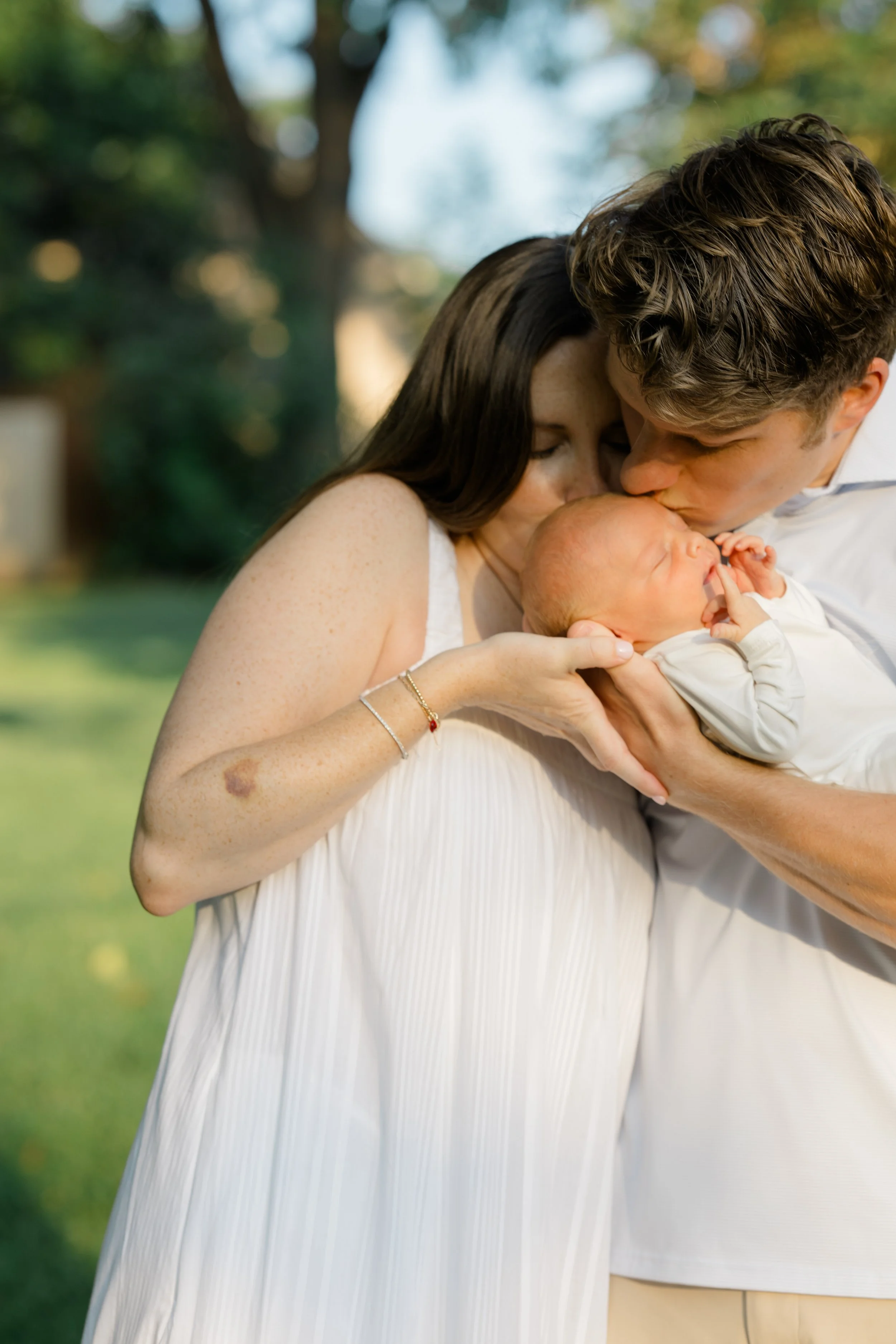 A woman and a man holding a newborn baby close to each other, outdoors.