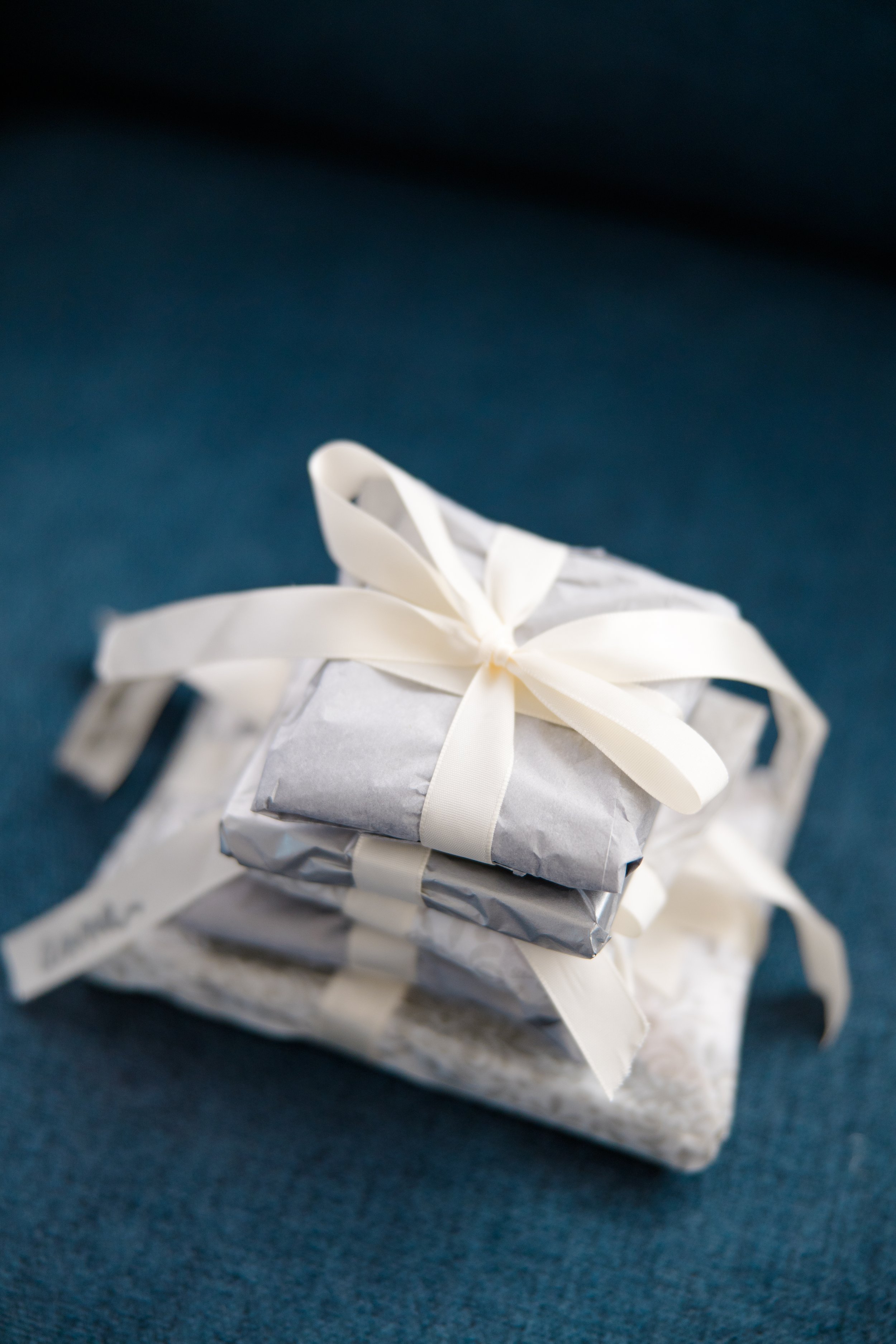 Two wrapped gifts, one with silver paper and a white ribbon, placed on a dark blue surface.