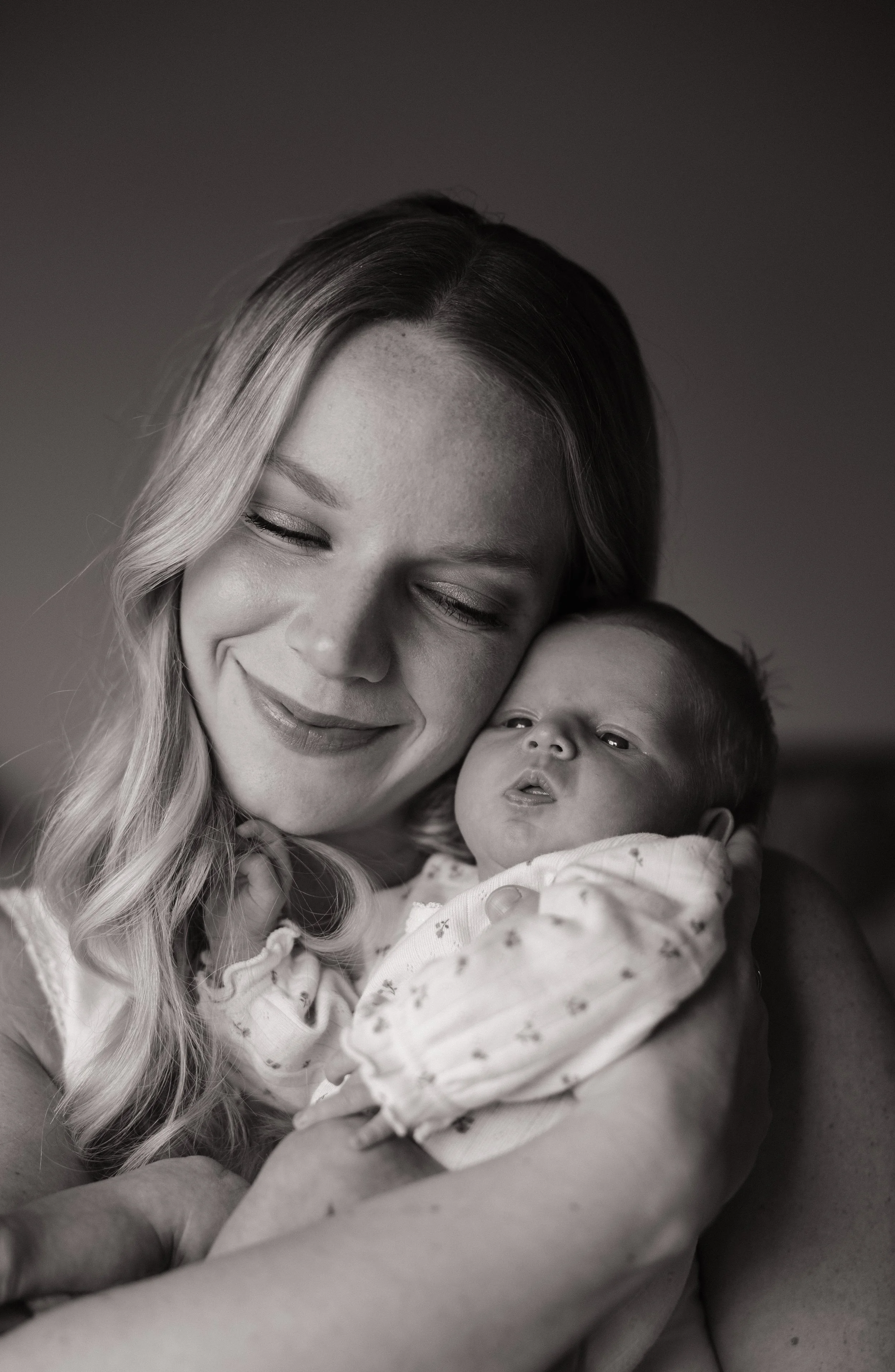 A woman with long wavy hair holding a baby. Both are smiling, and the photo is in black and white.