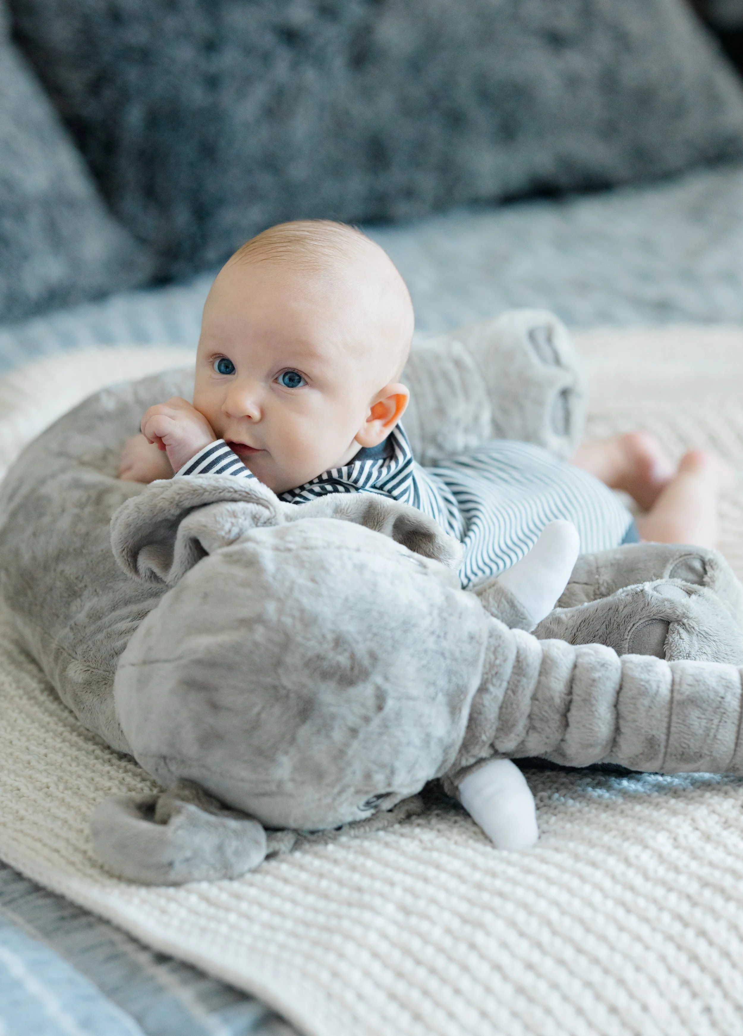 A baby with blue eyes and light hair lying on a plush blanket, wearing striped pajamas and socks, in a cozy indoor setting.