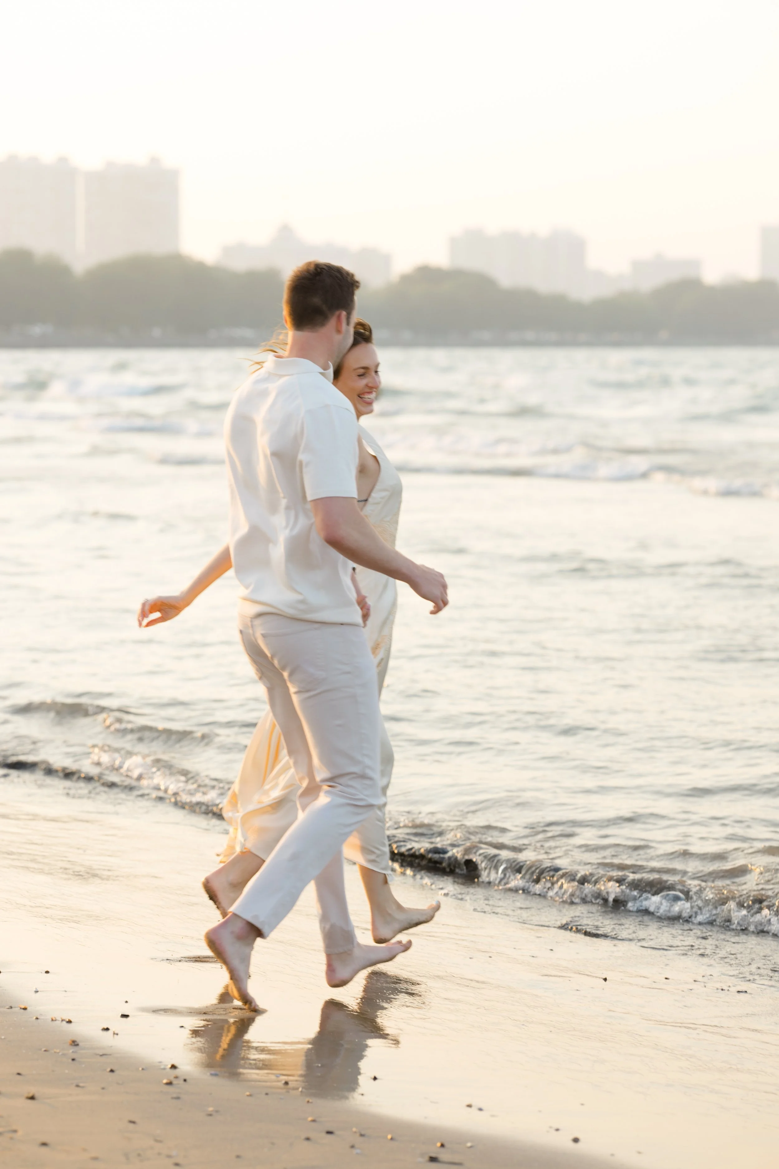 A couple walking barefoot along the shoreline at sunset, smiling and enjoying each other's company.