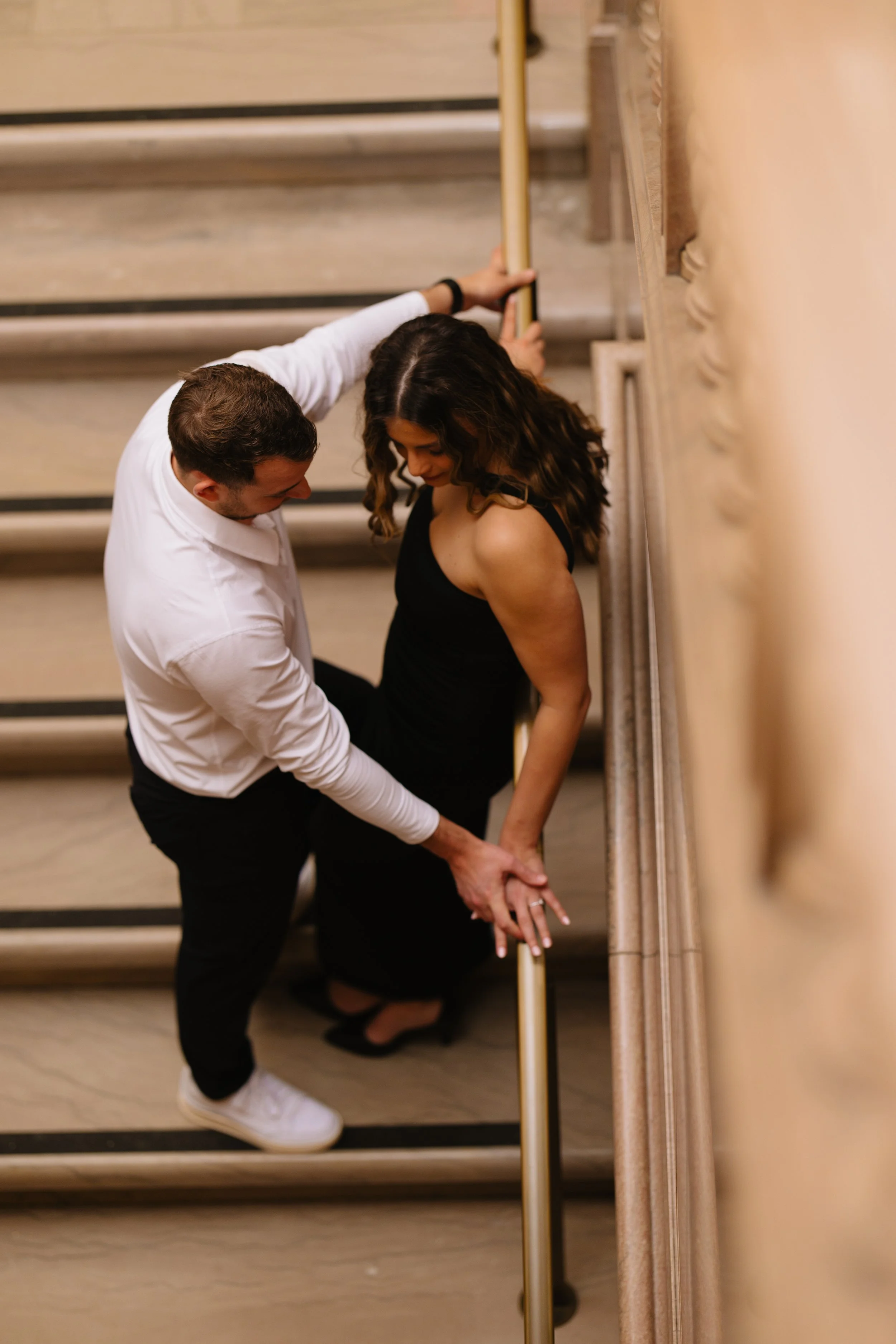 A man and woman holding hands and leaning against a staircase railing, with the man supporting the woman as she leans back.