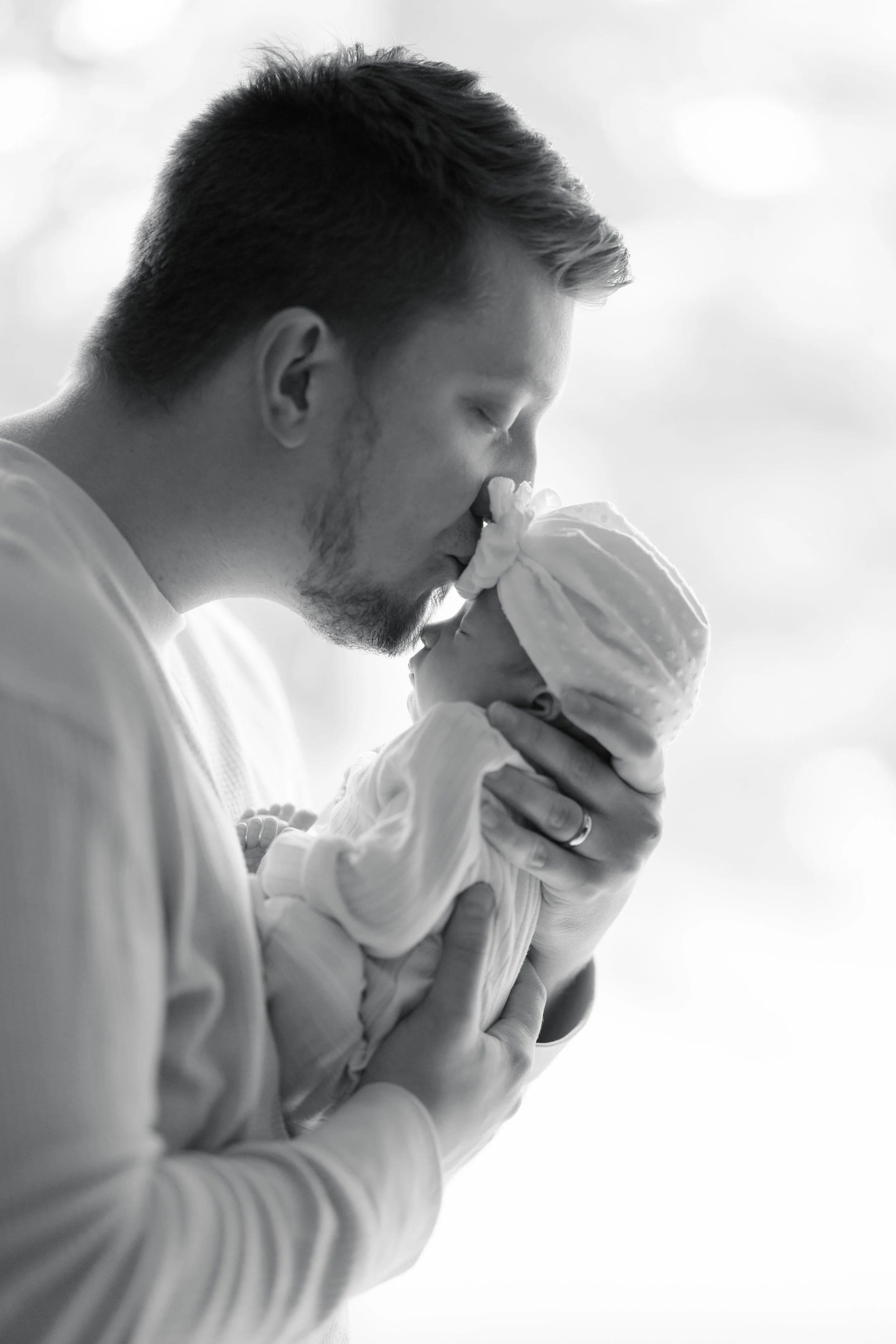 A man holds a sleeping baby close to his face, both with eyes closed, sharing a tender moment.