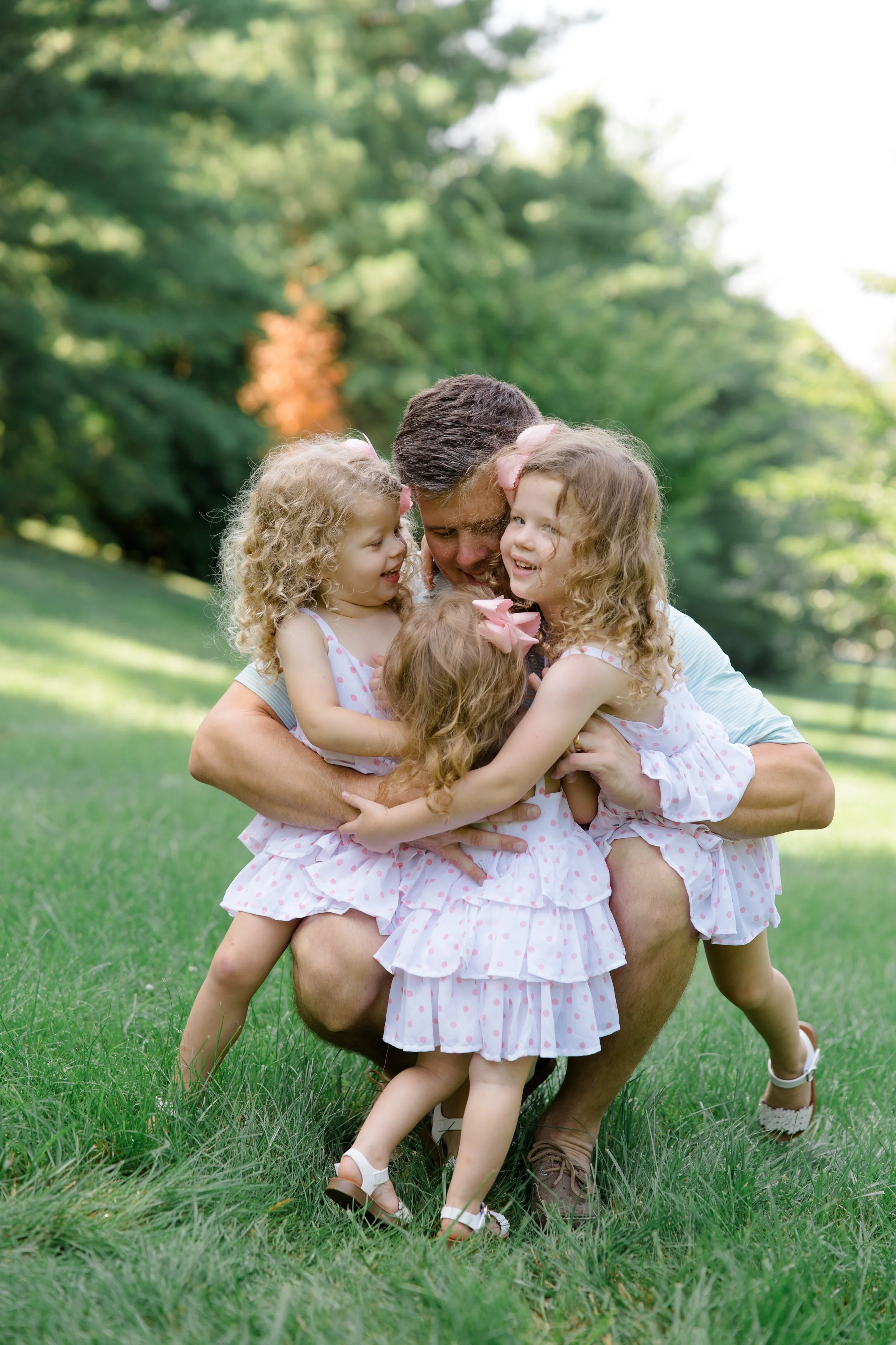 A man hugging four young girls outdoors on a grassy field with trees in the background.