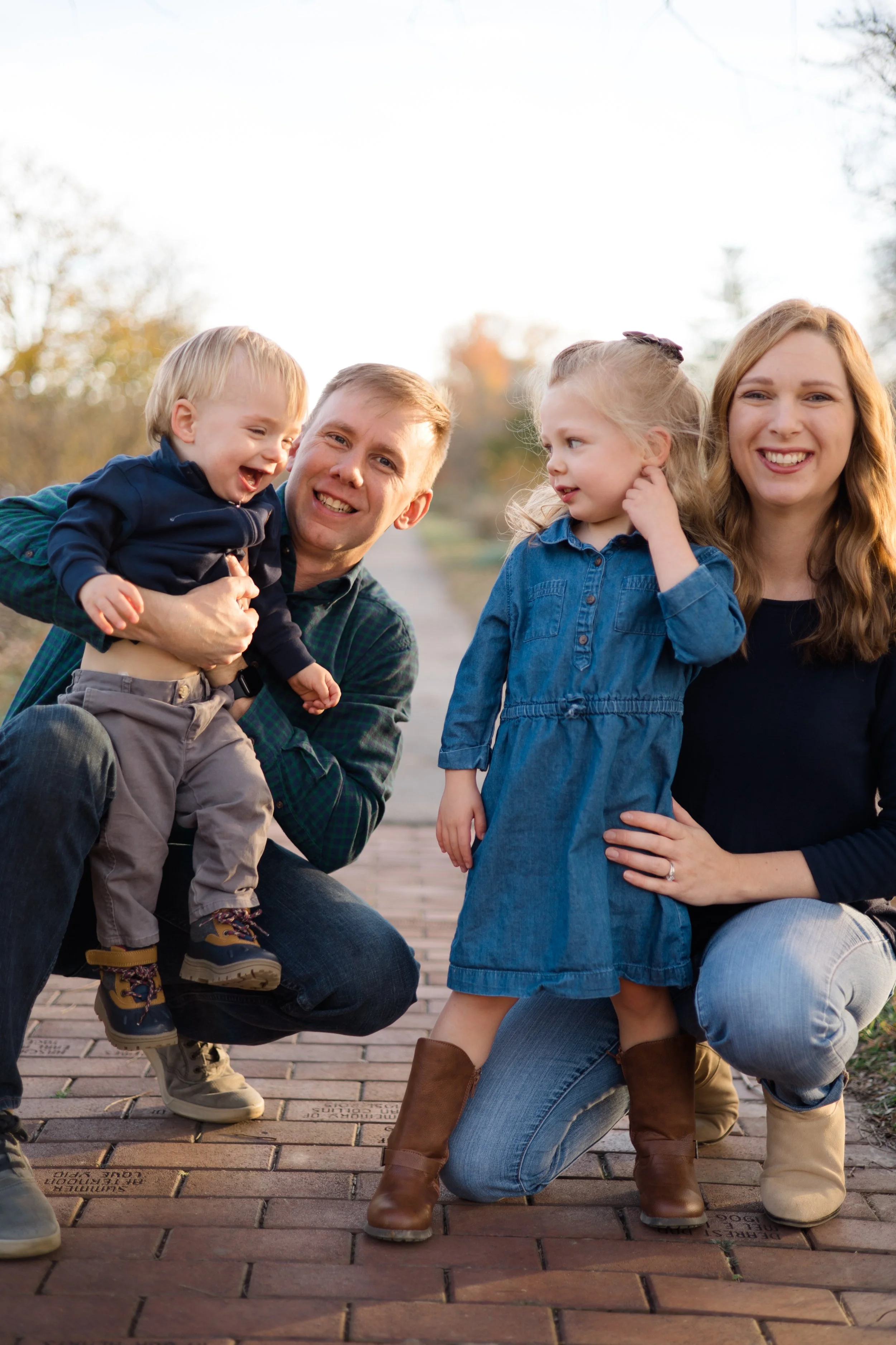 A family of four outdoors on a brick pathway, with children and parents smiling and enjoying each other's company.