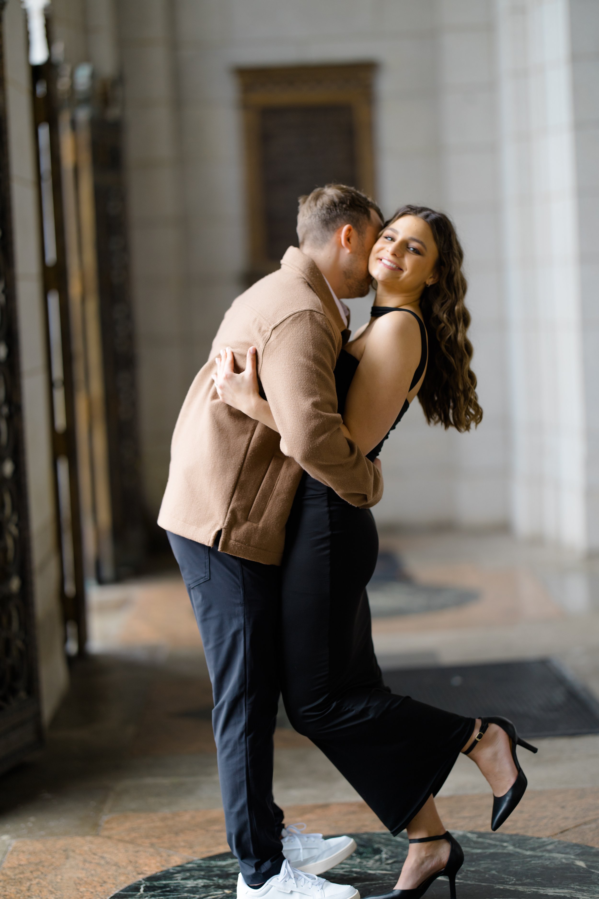 A couple dancing closely indoors with ornate architecture and marble walls, smiling and holding each other.