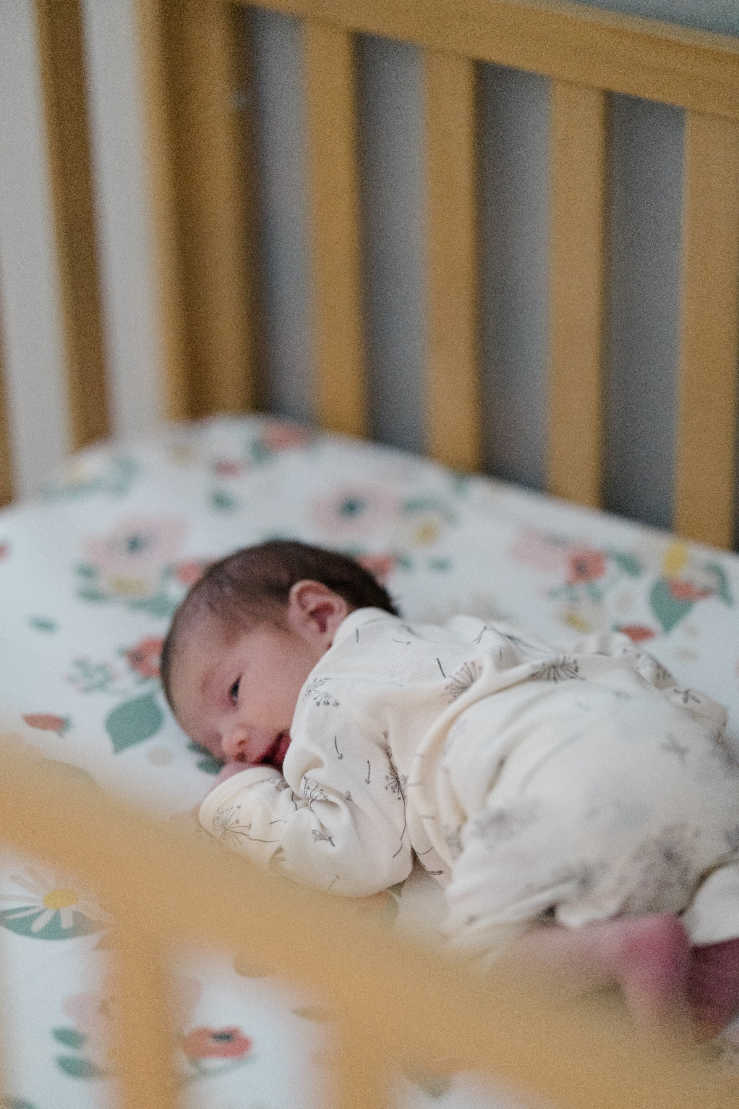 A baby lying in a crib with a floral sheet, looking towards the camera.