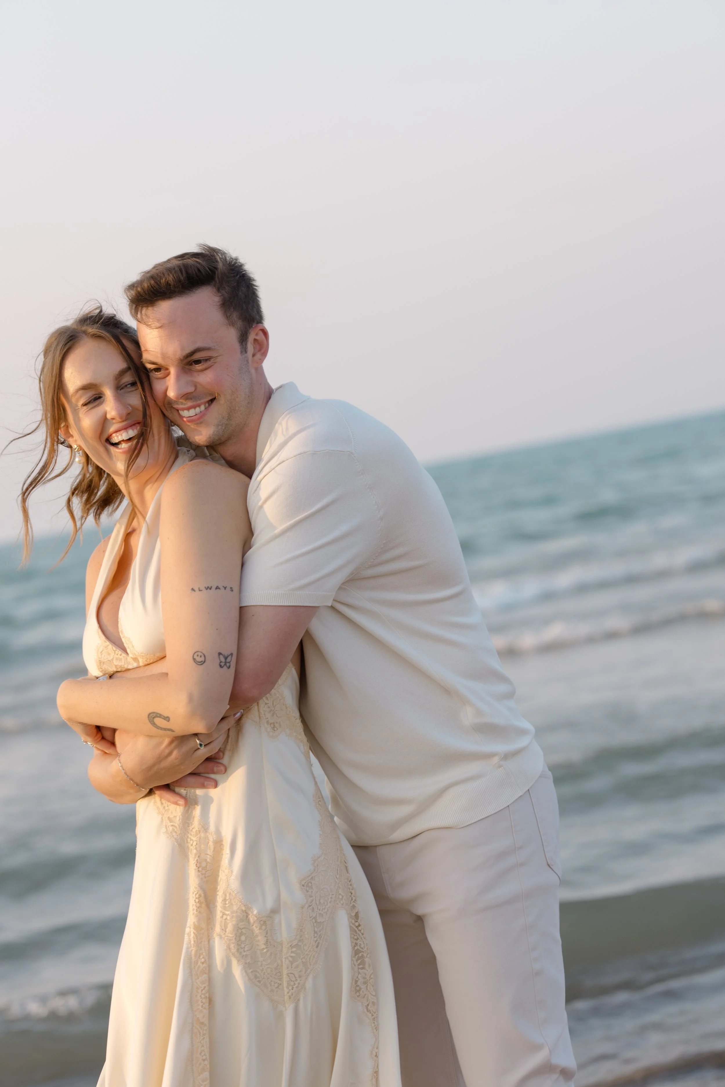 A happy couple standing on the beach with the ocean in the background, embracing and smiling.