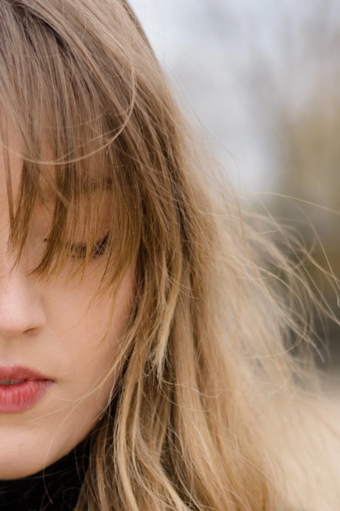 Close-up of a woman's face with blonde hair, covering one eye, with a neutral facial expression.