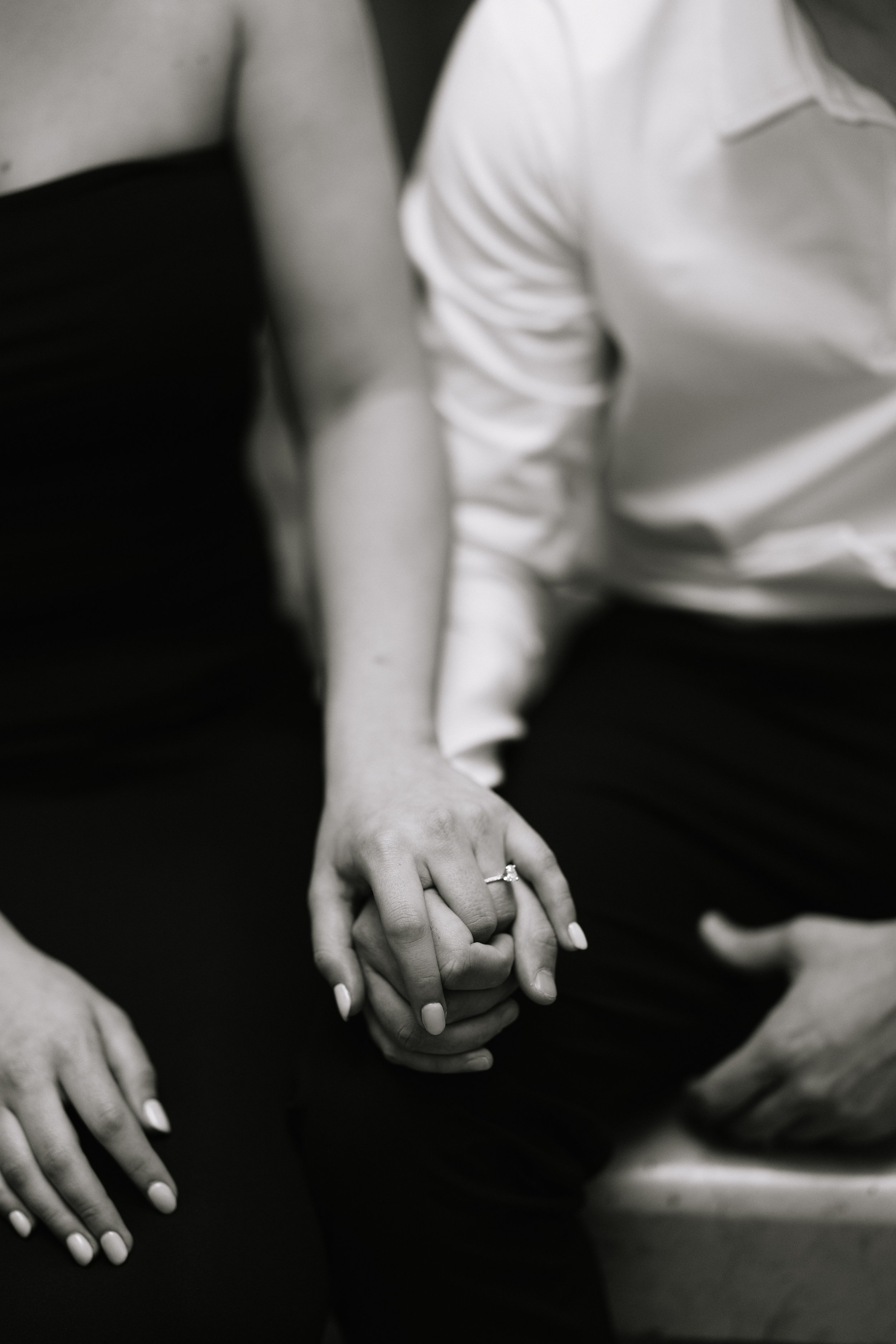 Close-up of hands joined together, with one person wearing a ring and white nail polish, in black and white.