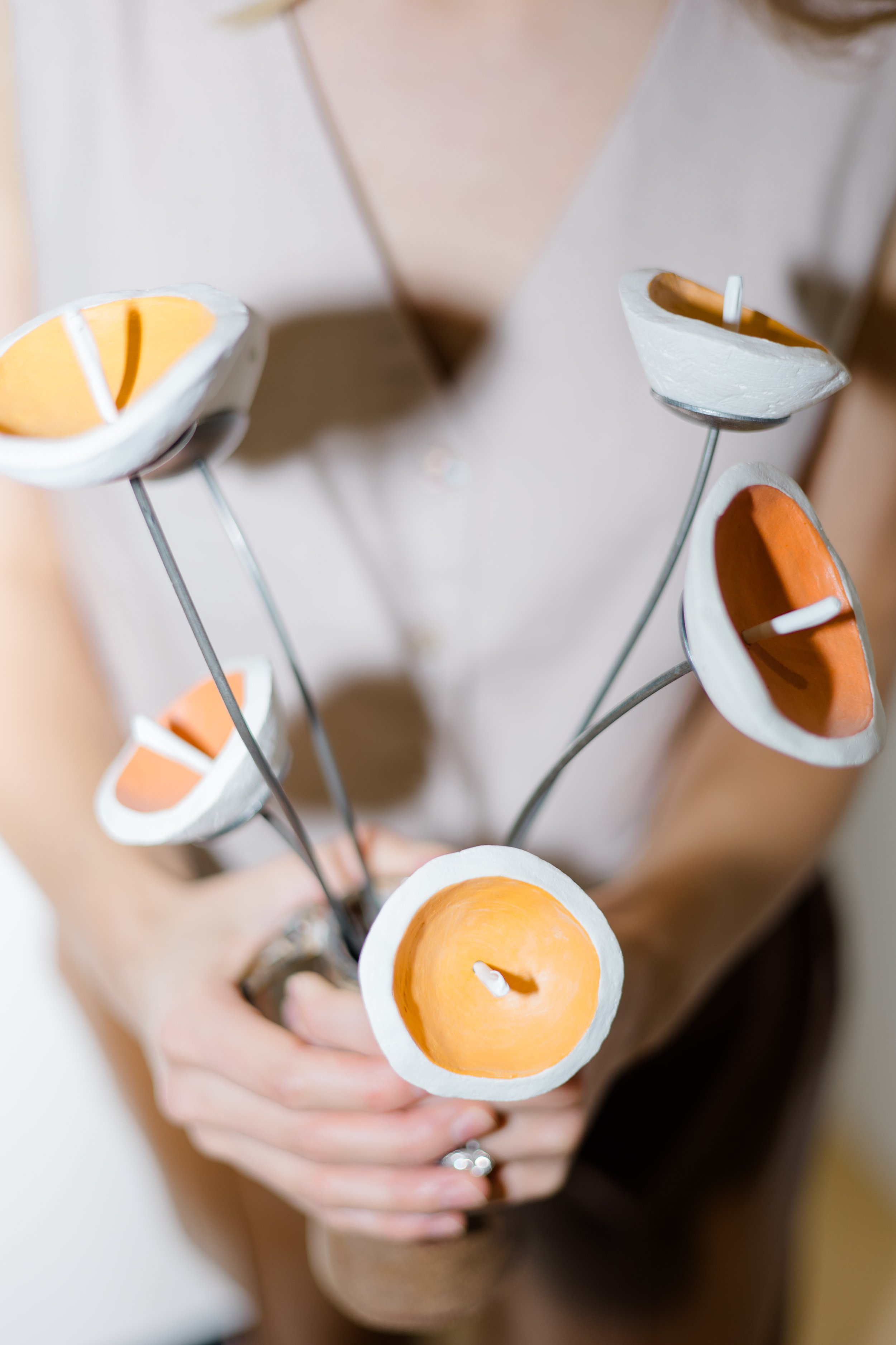 A person holding a decorative piece with several candle holders attached on metal stems, with orange and white candles inside.