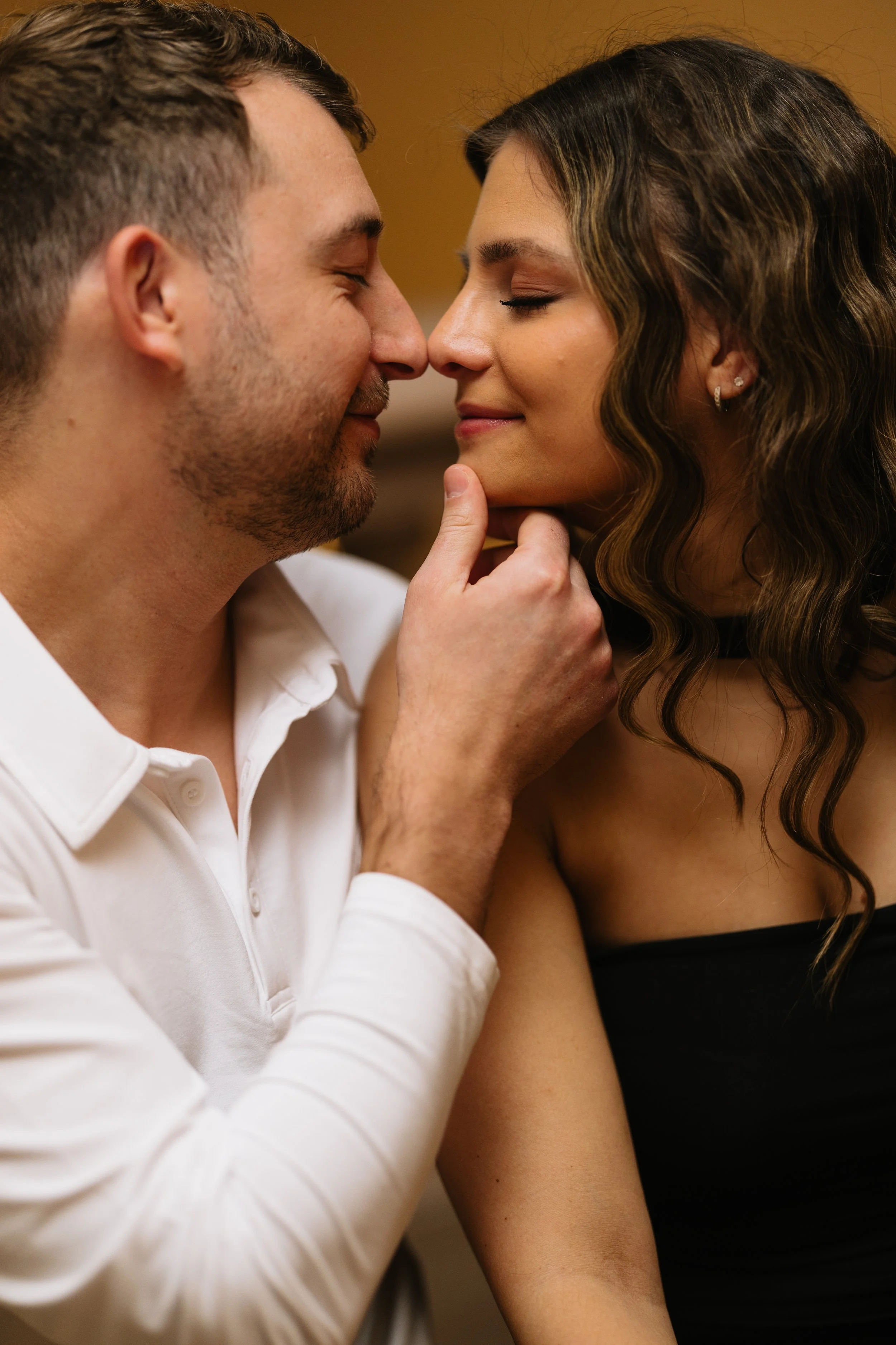 A close-up of a couple touching noses and smiling, with the woman gently holding the man's chin.