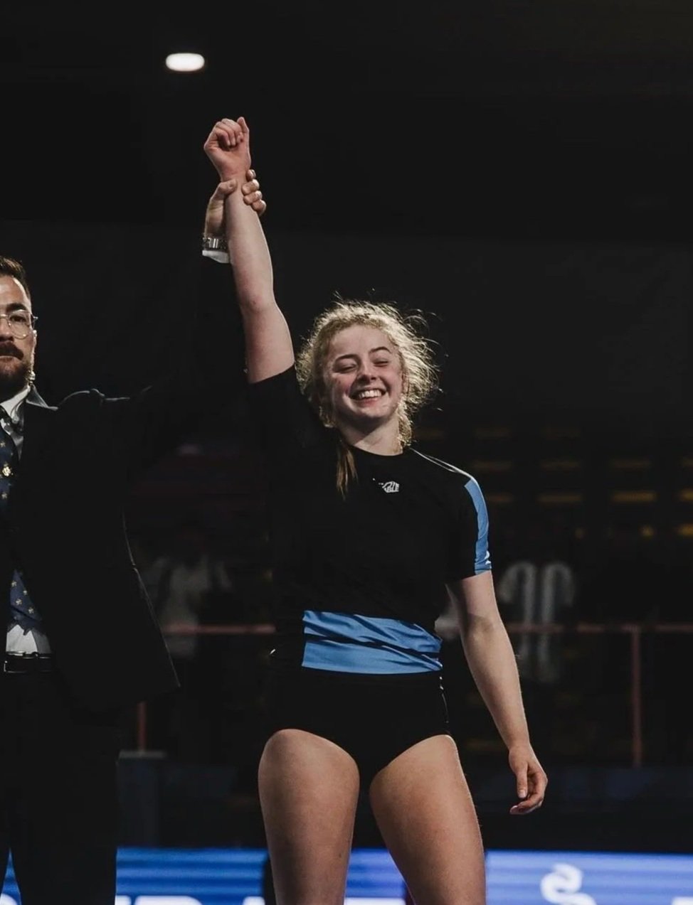 Vrouw in sportkleding die triomfantelijk met iemand anders haar hand omhoog houdt, lachend.
