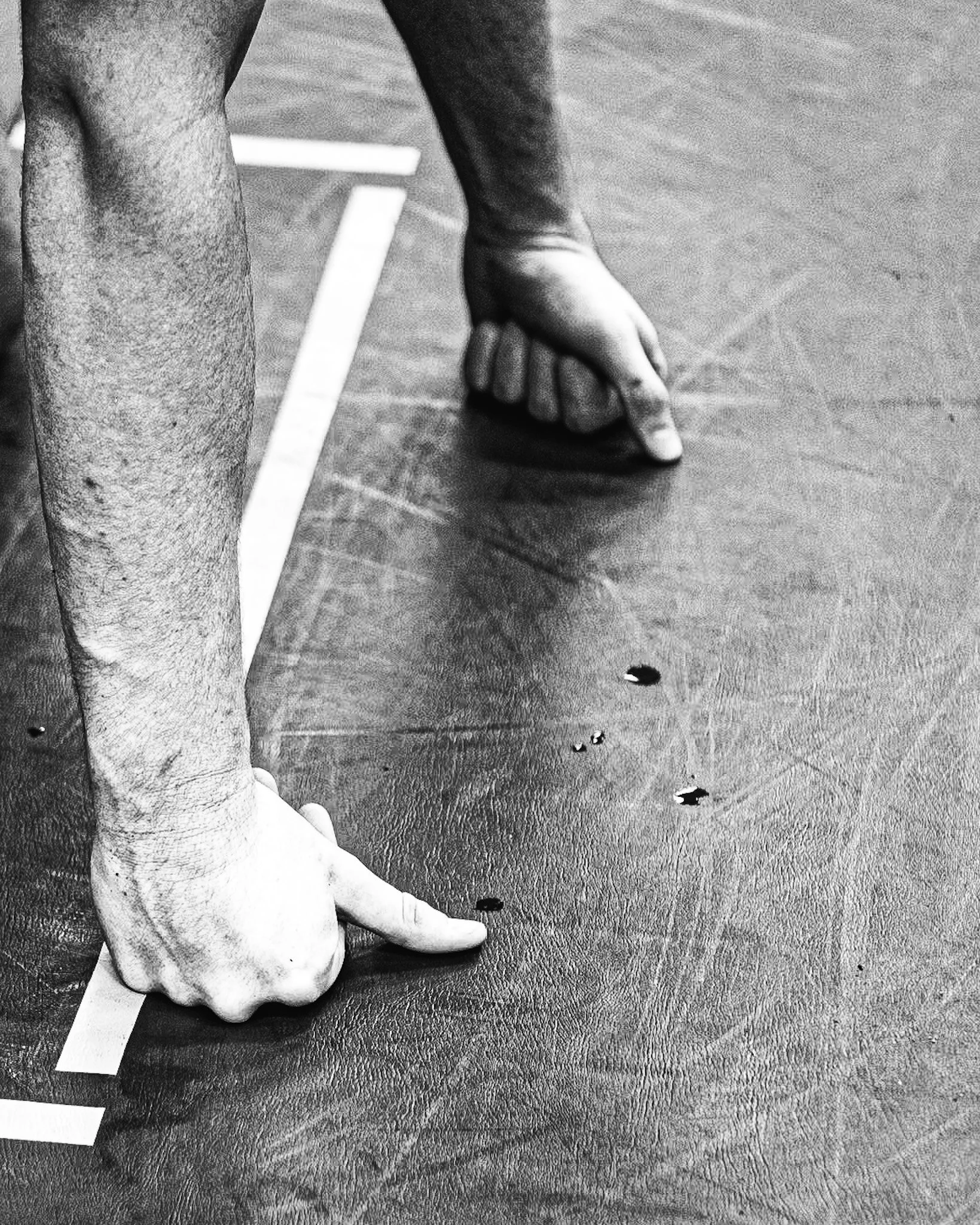 Black and white photo of a person's leg and foot on a textured surface, with their index finger pointing at a small dark spot on the surface nearby.