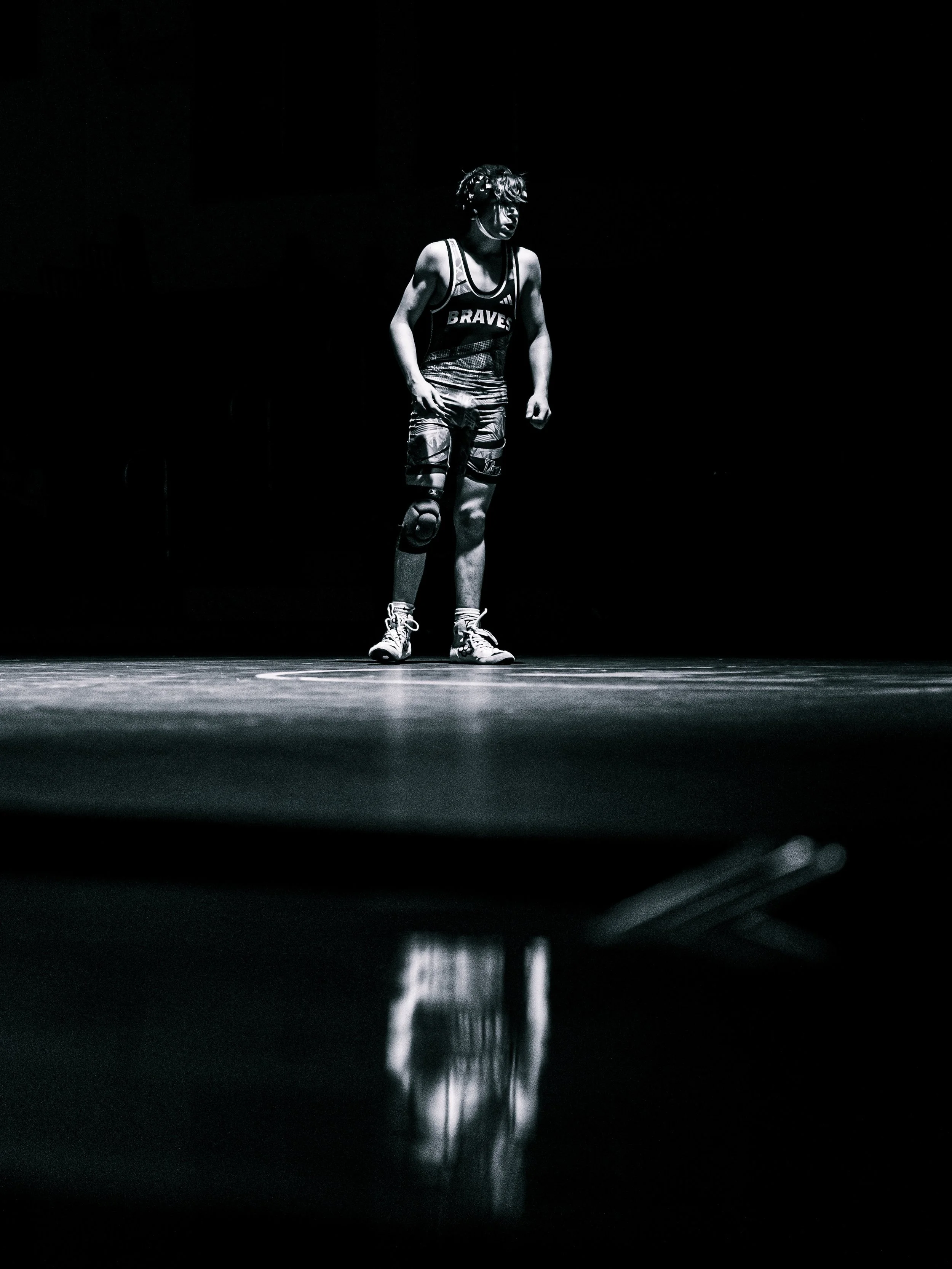 A young athlete wearing a sports jersey with the word 'BRAVES' stands in a spotlight on a dark stage, with a knee injury.