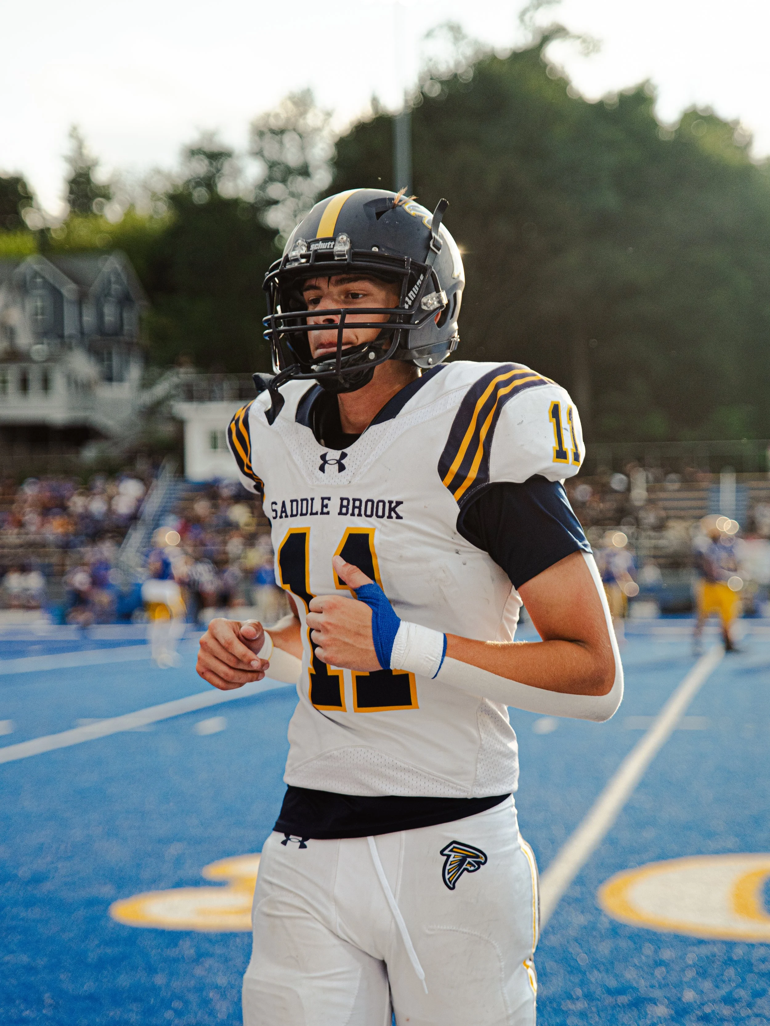 Young football player in a saddlebrook team uniform standing on a blue football field with a helmet on.