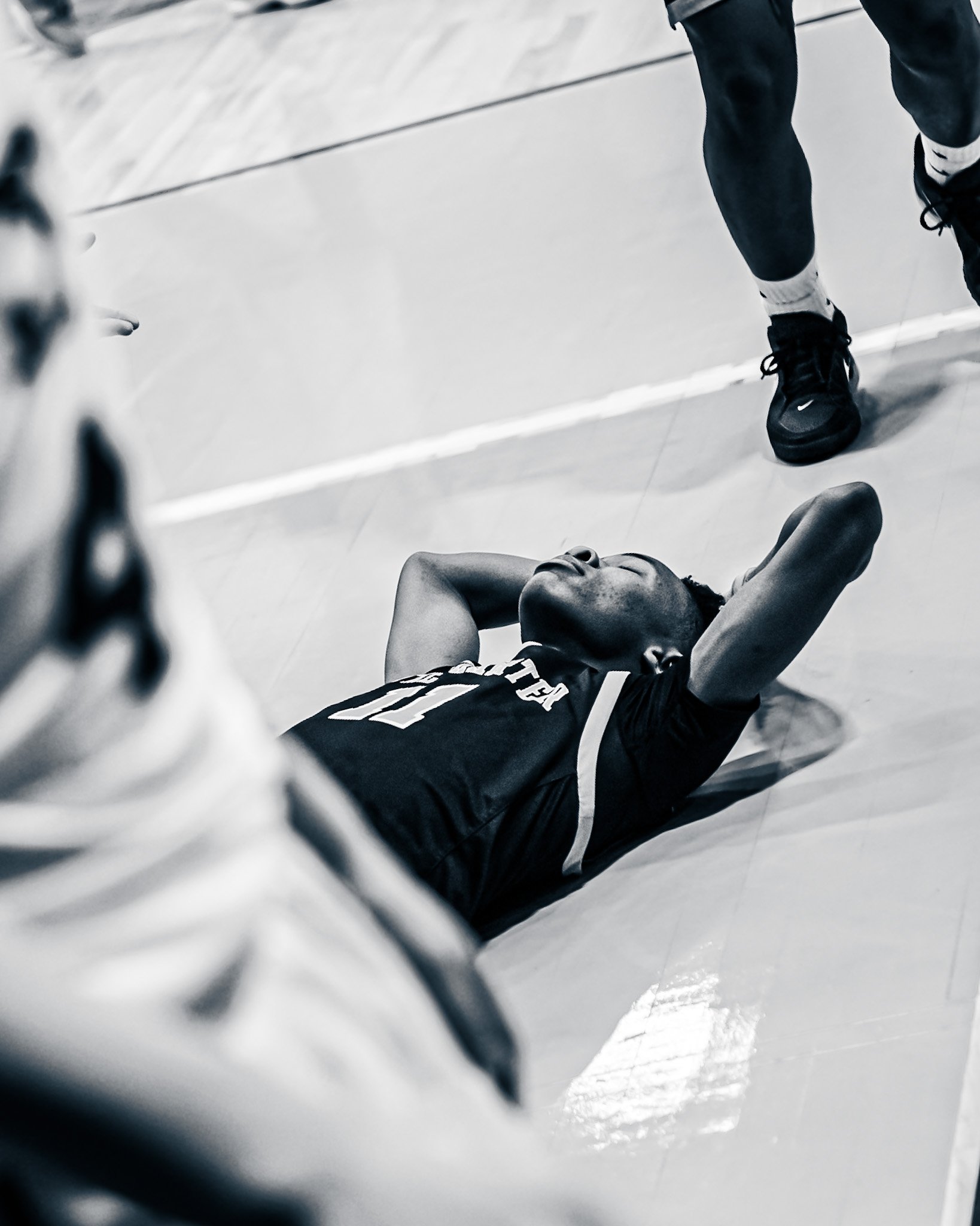 A person in black athletic shoes and socks running on a gym floor, viewed through a chain-link fence.