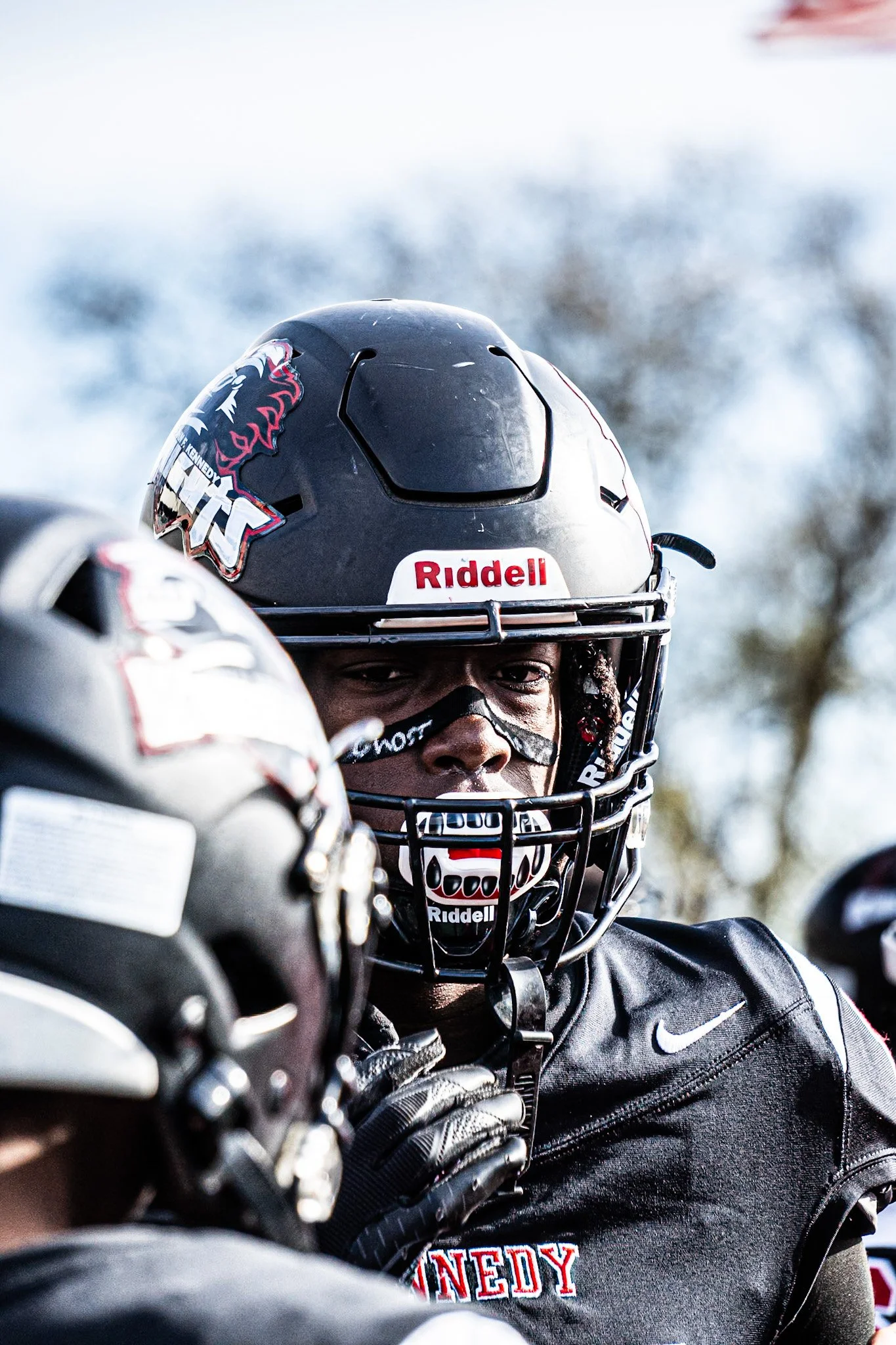 Close-up of a football player wearing a black helmet with stickers and a faceguard, looking directly at the camera.