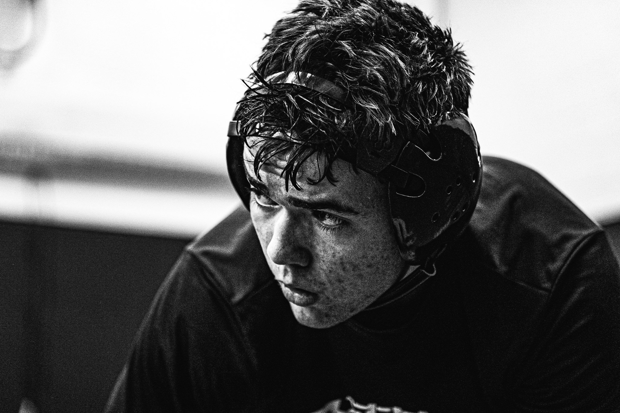 A close-up black-and-white photograph of a young man with wet curly hair wearing headphones, looking downward.