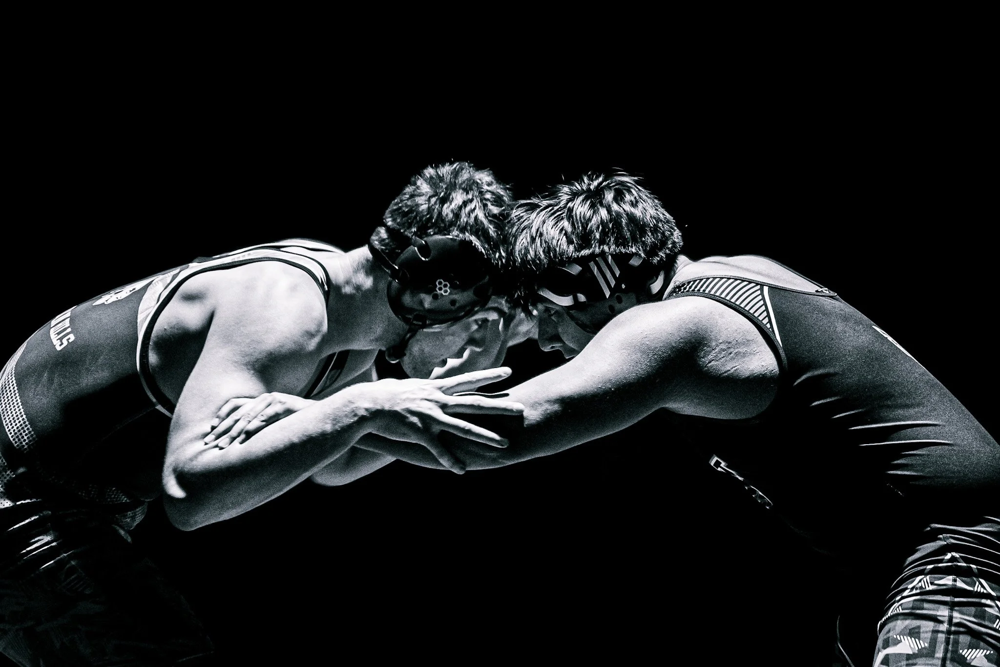 Two wrestlers in black and white, facing each other, touching foreheads in a wrestling hold.