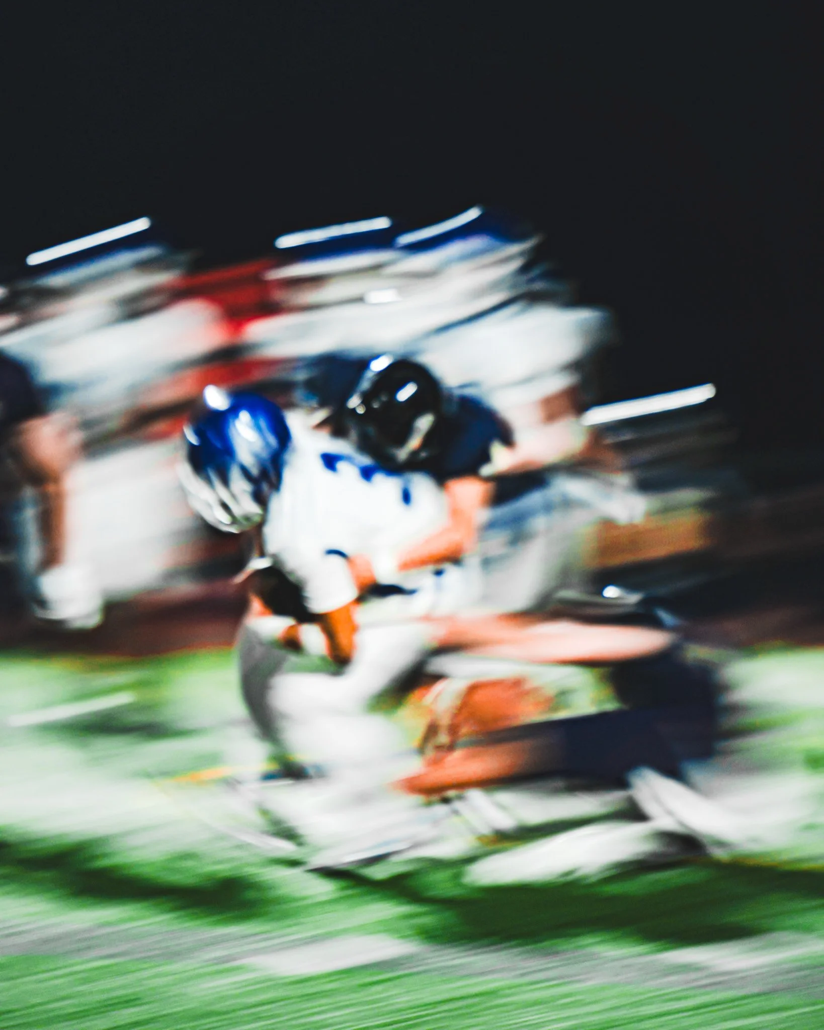 Blurred image of a person riding a motorcycle on a racetrack at night, with blurred stadium lights in the background.