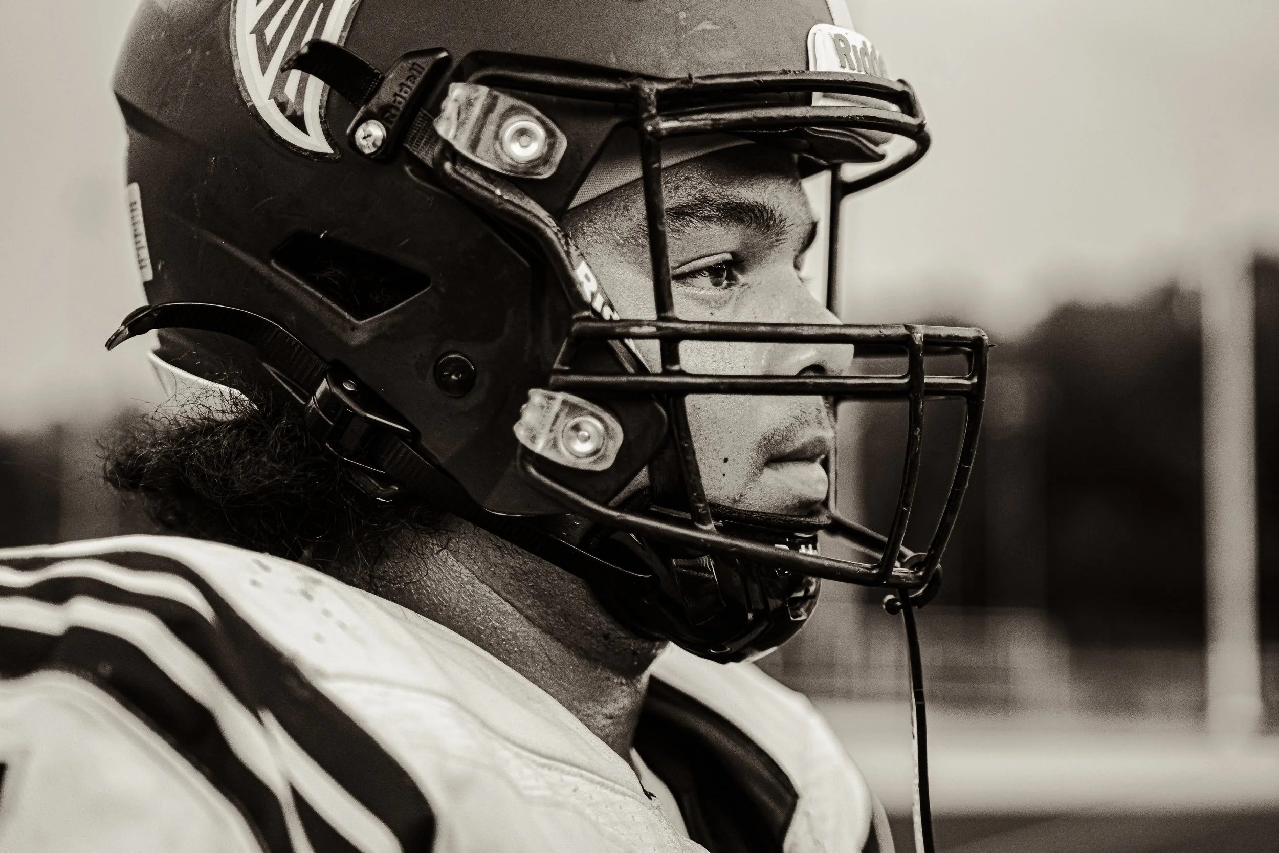A football player wearing a helmet with a faceguard. The faceguard is black, and the player is looking to the right, showing part of his face and eye. The helmet has a logo and some text on it. The player is dressed in a sports uniform, with a part o