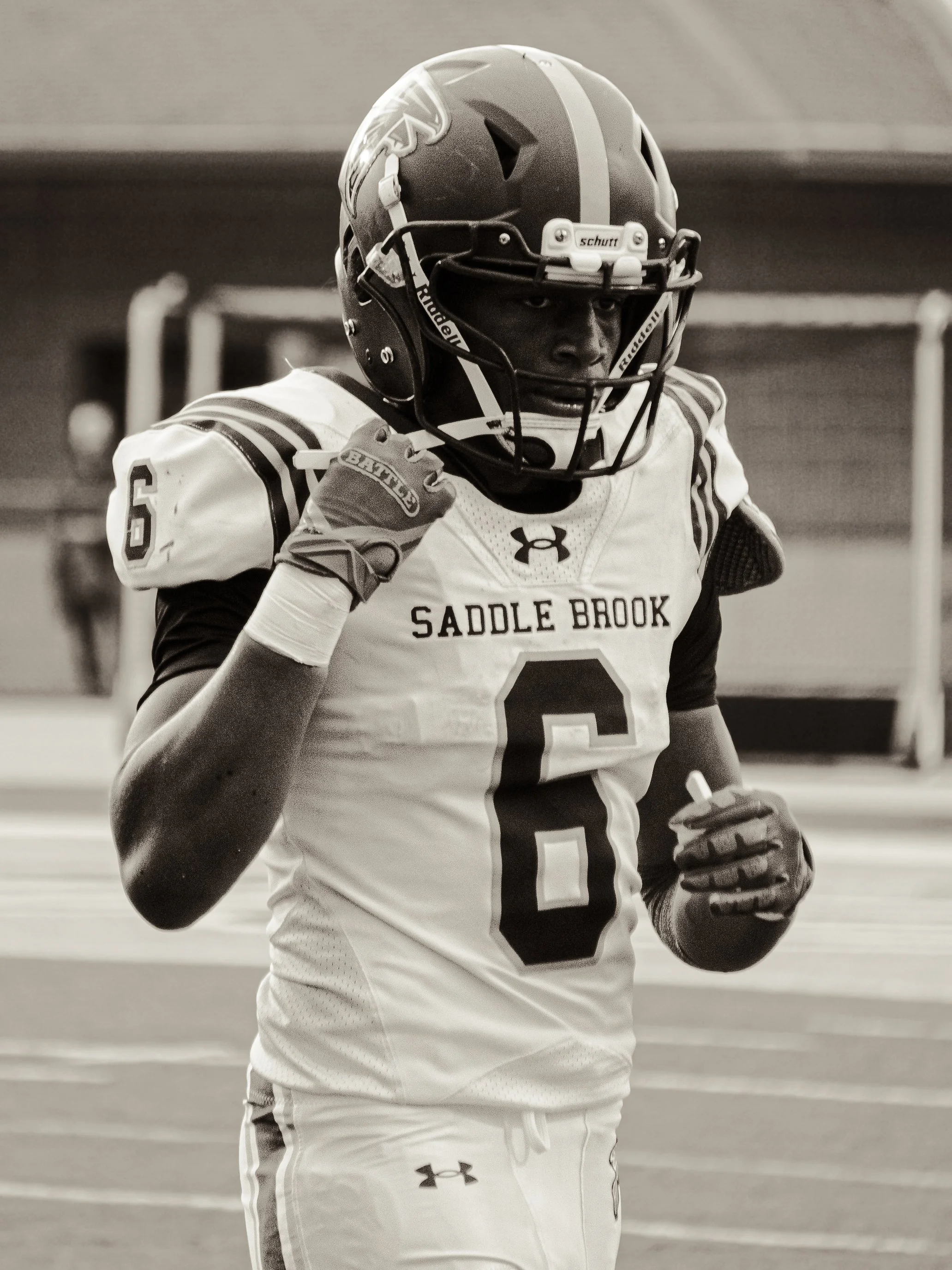 A football player wearing a helmet, gloves, and jersey on a field with bleachers in the background.